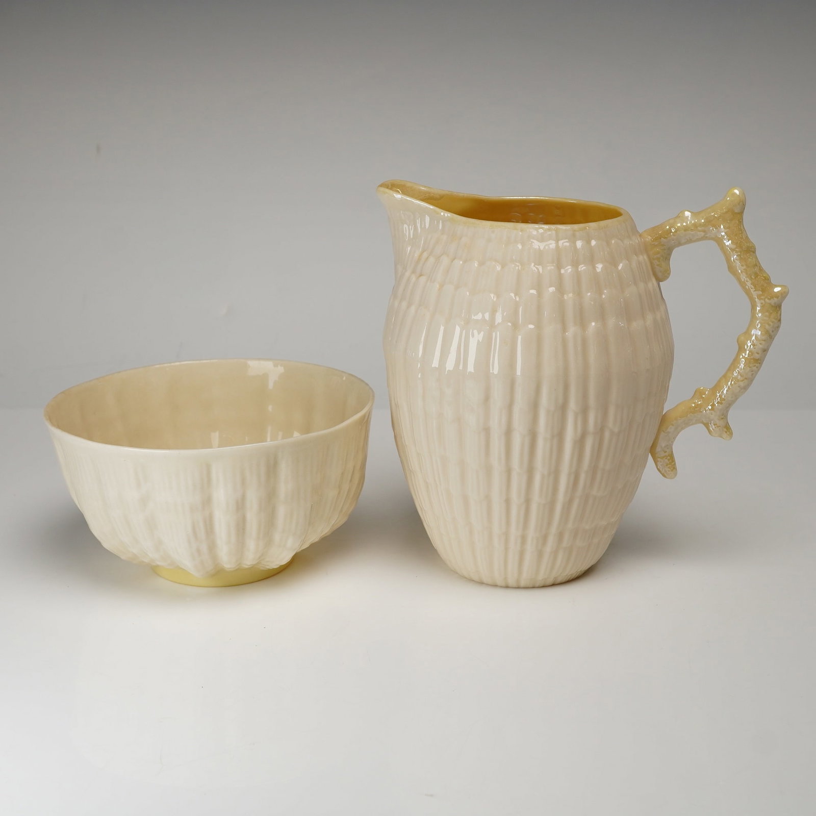 Belleek Neptune Pattern Parian Porcelain Creamer and Sugar Bowl: A pair of Belleek Parian porcelain tablewares in the Neptune pattern, comprising an open sugar bowl and a matching creamer. Each piece features a finely molded body with shell-like ribbing and a