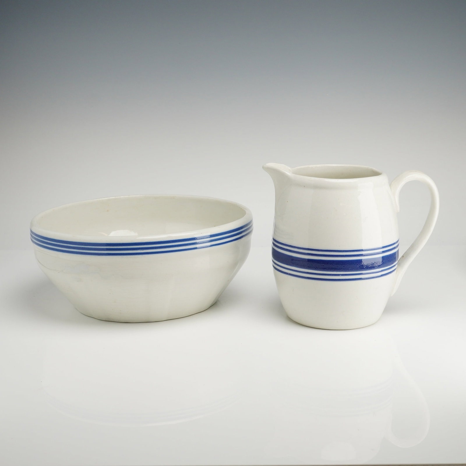 USA Heritage Blue Stripe Stoneware Pitcher and Bowl Set: A two-piece Heritage Blue Stripe stoneware set comprising a pitcher and a bowl. The white ceramic bodies are decorated with a pattern of three parallel horizontal blue stripes encircling the exterior,