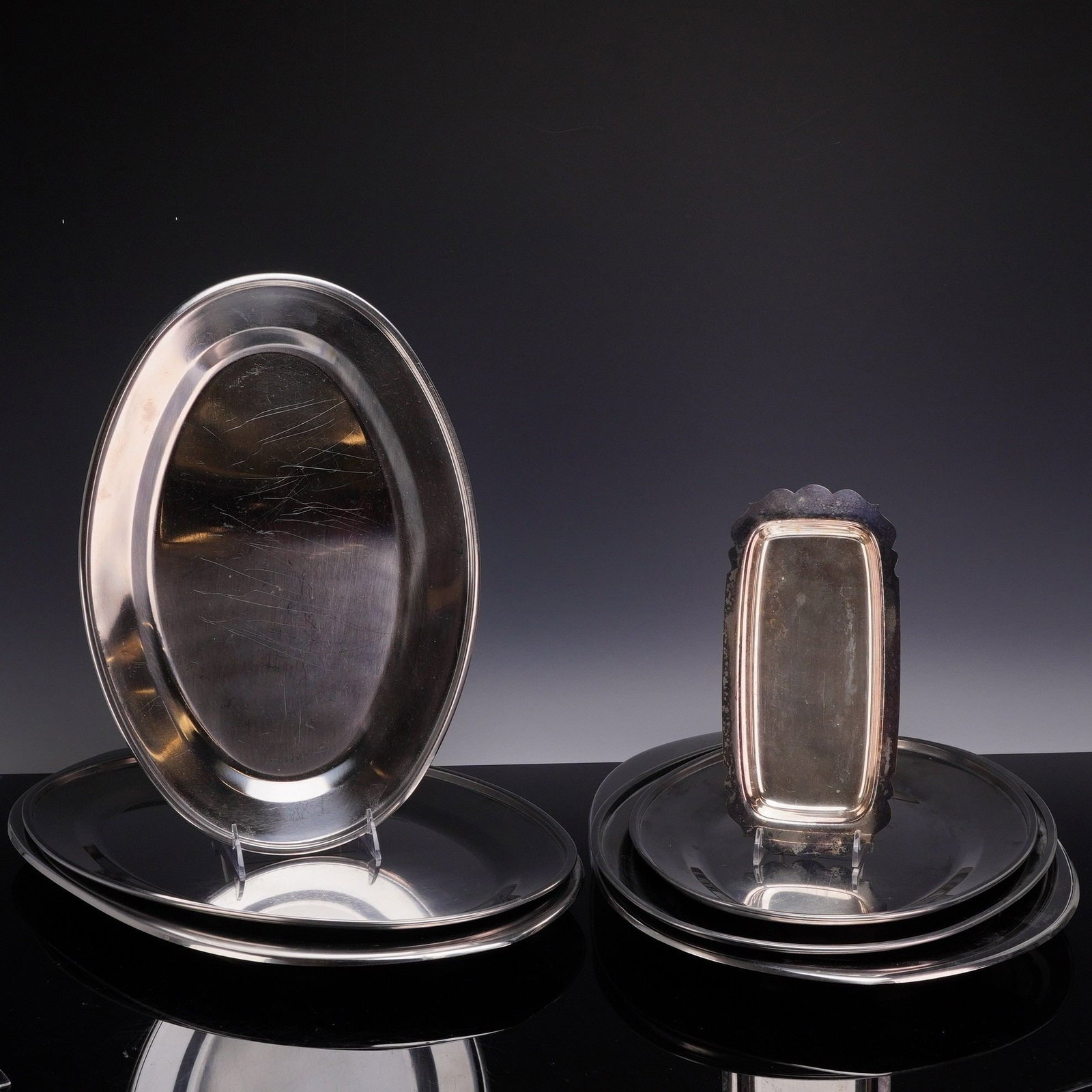 Set of 7 Stainless Steel Platters and a Scalloped Serving Dish: The group includes 7 platters of graduated sizes in both oval and round shapes, along with a small rectangular serving dish. Each item is constructed from polished stainless steel and features a