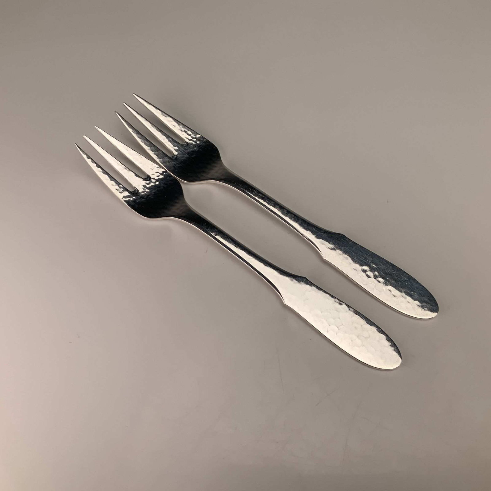 A Pair of Georg Jensen Denmark EPNS Mermaid Pattern Hammered Fish Forks: This pair of fish forks is manufactured by Georg Jensen of Denmark in the Mermaid pattern. The items are constructed from electroplated nickel silver, as indicated by the EPNS designation. The design