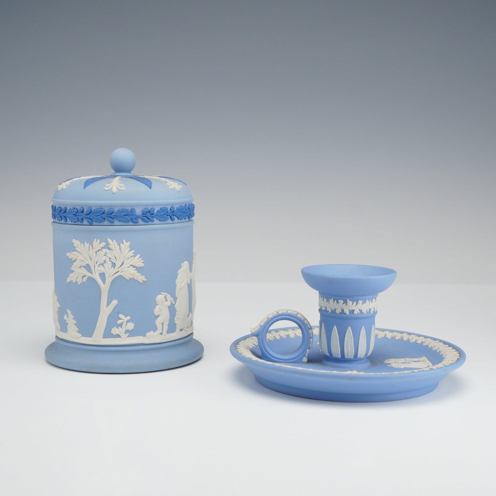 2pc Wedgwood Pale Blue Jasperware: This lot consists of two pieces of Wedgwood pale blue jasperware, a fine-grained, unglazed stoneware featuring sprigged white bas-relief neoclassical decoration. The first item is a covered cylindrica