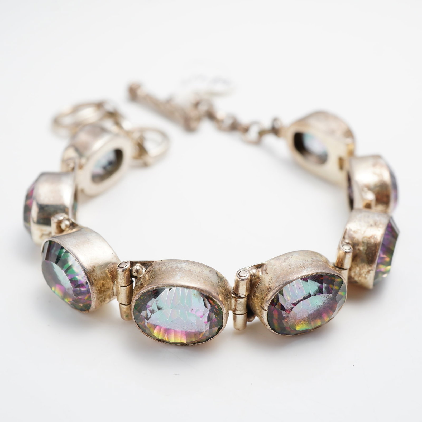 Sterling Silver and Mystic Amethyst Link Bracelet: This sterling silver link bracelet features nine oval-cut amethyst gemstones, each treated with an iridescent multi-color coating to create a mystic finish. The stones are individually set in oval bez