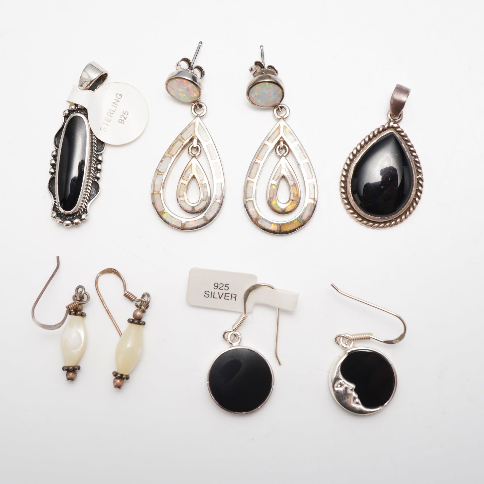 8-Piece Collection of Sterling Silver Jewelry Including Three Pairs of Earrings and Two Pendants: This eight-piece collection of sterling silver jewelry consists of three pairs of earrings and two pendants, featuring black onyx, iridescent synthetic opal, and mother-of-pearl accents. The first pen