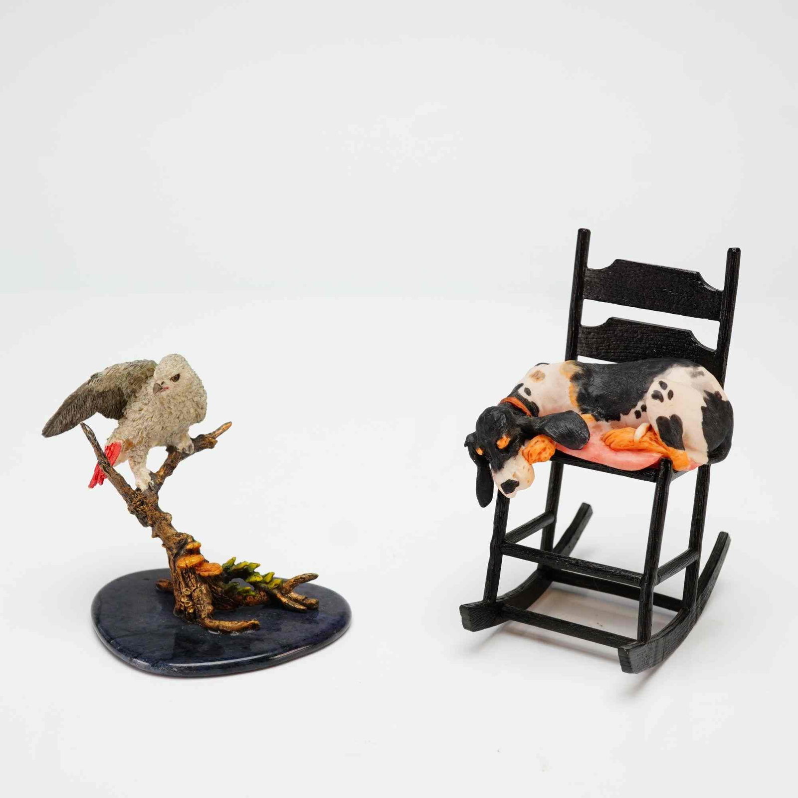A Pair of Schmid and Tropical Paradise Figurines, Sawin' Logs and African Gray Parrot: This lot features two small collectible animal figurines. The first is a Lowell Davis (1937??"2020) figurine titled Sawin' Logs, which depicts a tricolor spotted hound dog sleeping on a pink cushion. 