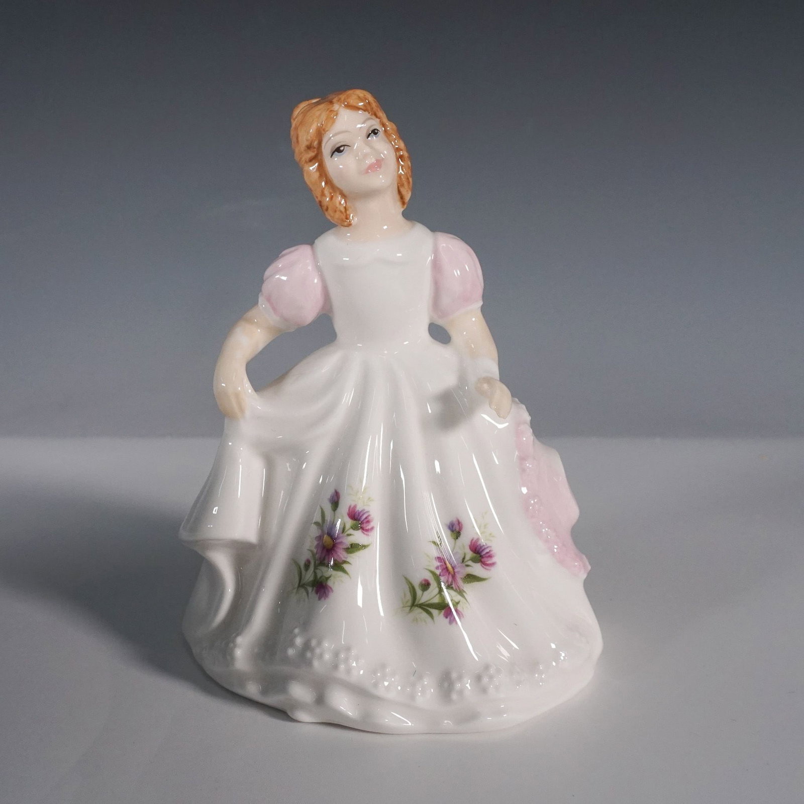 Royal Doulton Figure of the Month, September HN3326: Part of the Flower of the Month series. This charming porcelain figurine showcases a young girl in an elegant white dress adorned with delicate lilac flowers, complemented by pink puffed sleeves and a