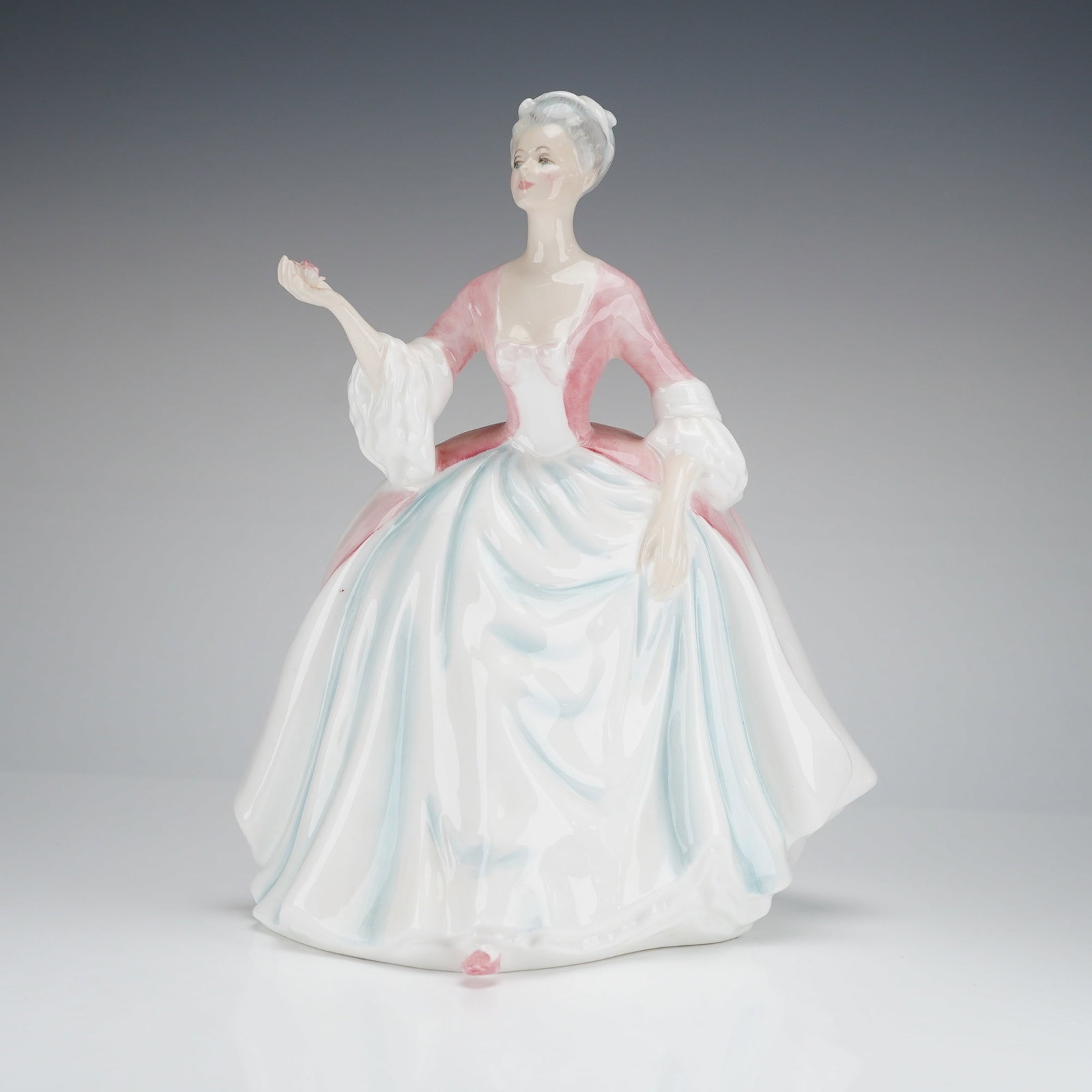 Royal Doulton Figurine Diana HN3266: The figure, modelled by Peggy Davis, depicts a woman in an 18th-century influenced dress, featuring a pink bodice and a voluminous white skirt accented with pale blue shadowing. The figure has grey ha