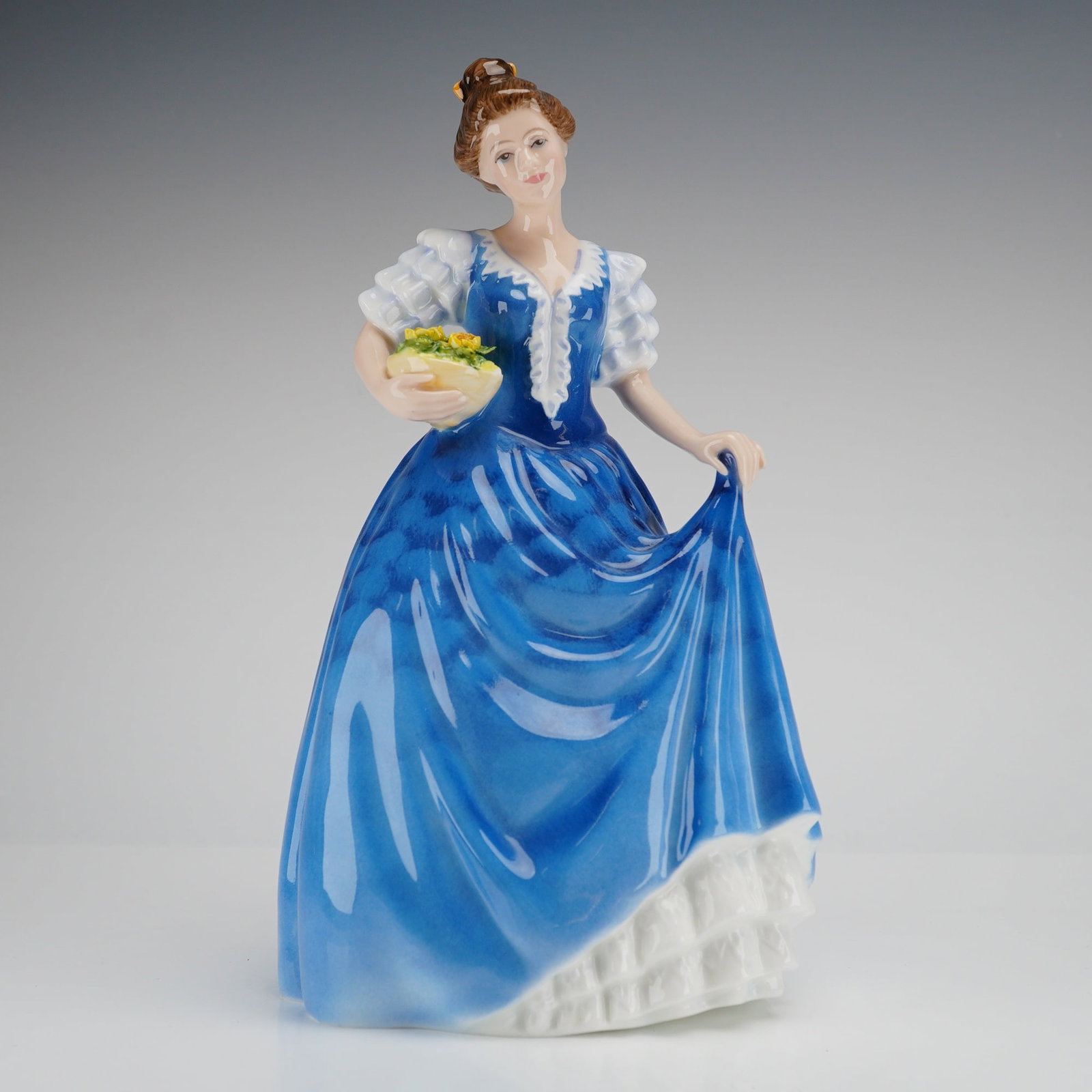 Royal Doulton Figurine Helen HN3601: A Royal Doulton Figurine, Helen HN3601, modeled by Amanda H. Treloar in 1993, depicting a woman in a blue and white dress holding a basket of yellow flowers. Dimensions: 4.50"L x 4.00"W x 8.50"H Weigh
