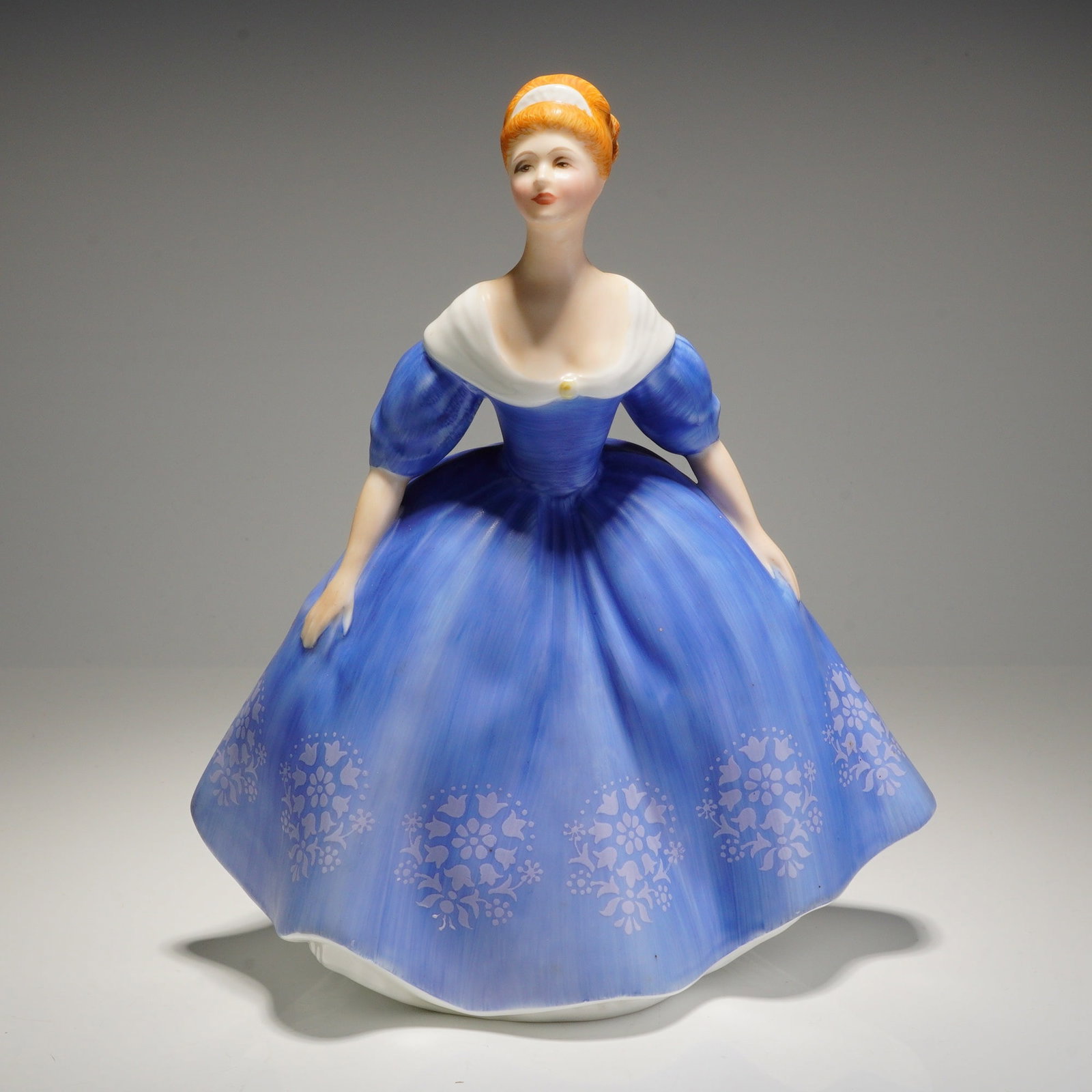 Royal Doulton Figurine Nina HN2347: A glazed bone china figurine, depicting a woman in a blue and white dress, with a floral pattern along the bottom of the skirt. The underside features the Royal Doulton backstamp, the title 'Nina', an