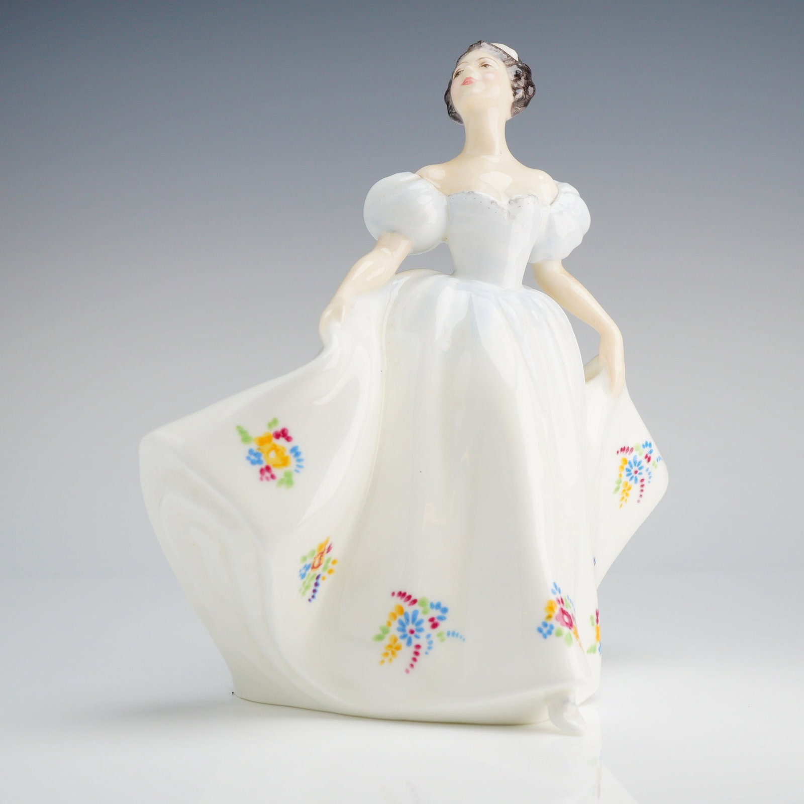 Royal Doulton Figurine, Kate HN2789: The figure depicts a female subject in a historical style, posed as if dancing or curtsying, wearing a flowing white gown with large, puffed sleeves. The skirt is decorated with polychrome hand-painte
