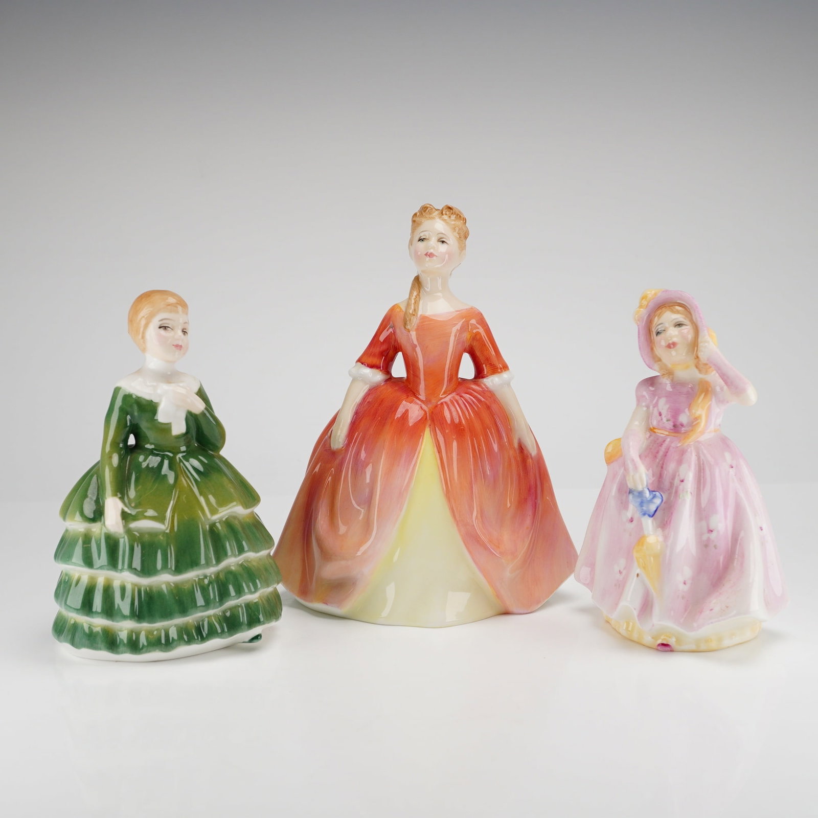 Three Royal Doulton Porcelain Figurines: Debbie, Babie, and Belle: A collection of three Royal Doulton porcelain figurines, including Debbie HN2400, Babie HN2121, and Belle HN2340, with the largest figure, Debbie, signed by Michael Doulton on May 3rd 1985. Dimensions