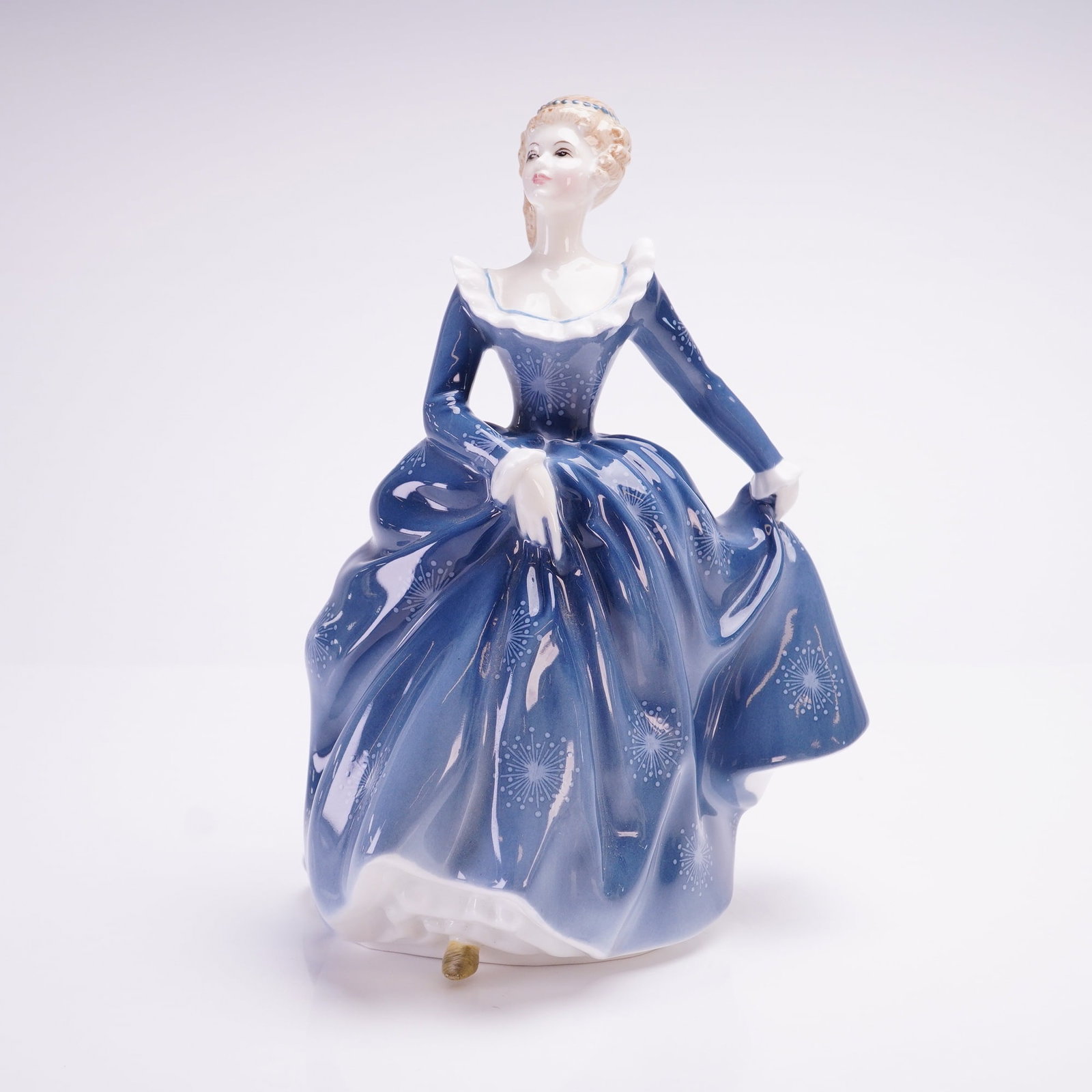 Royal Doulton Bone China Figurine, Fragrance HN2334: A Royal Doulton bone china figurine titled Fragrance, model HN2334. This glazed figure depicts a woman in a deep blue eighteenth-century style gown decorated with white starburst patterns and a ruffle