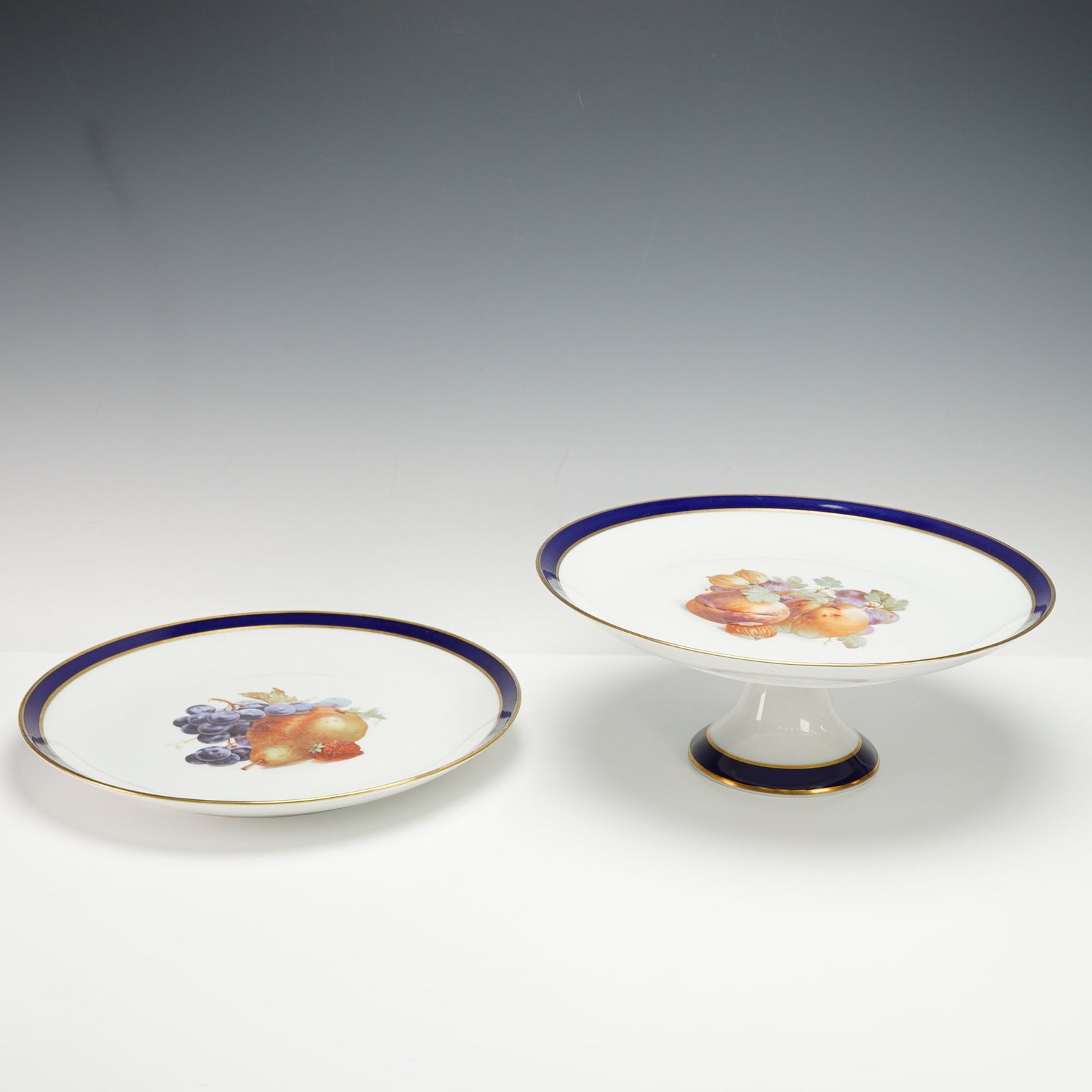 2pc Schumann Arzberg Porcelain Footed Platter and Round Platter, Bountiful: Schumann Arzberg Bavaria porcelain serving pieces in the Bountiful pattern, including a footed platter and a large round platter, each with cobalt blue borders, gilt trim, and multicolor fruit