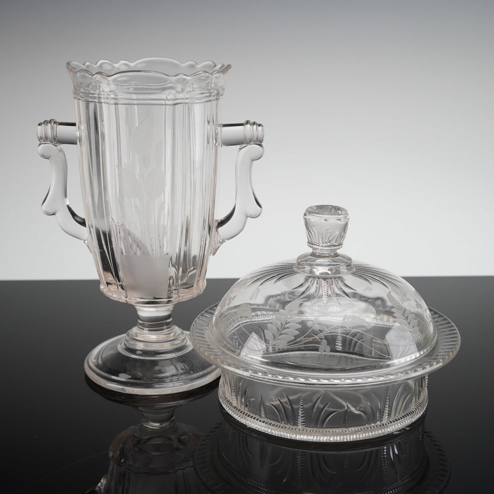 2pc Bryce Higbee Paneled Vase and Covered Dish: The handled vase is footed with a ribbed body, heavy molded handles, and a scalloped rim, featuring frosted stylized leaf motifs on the front panel. The covered round dish comprises a base with molded