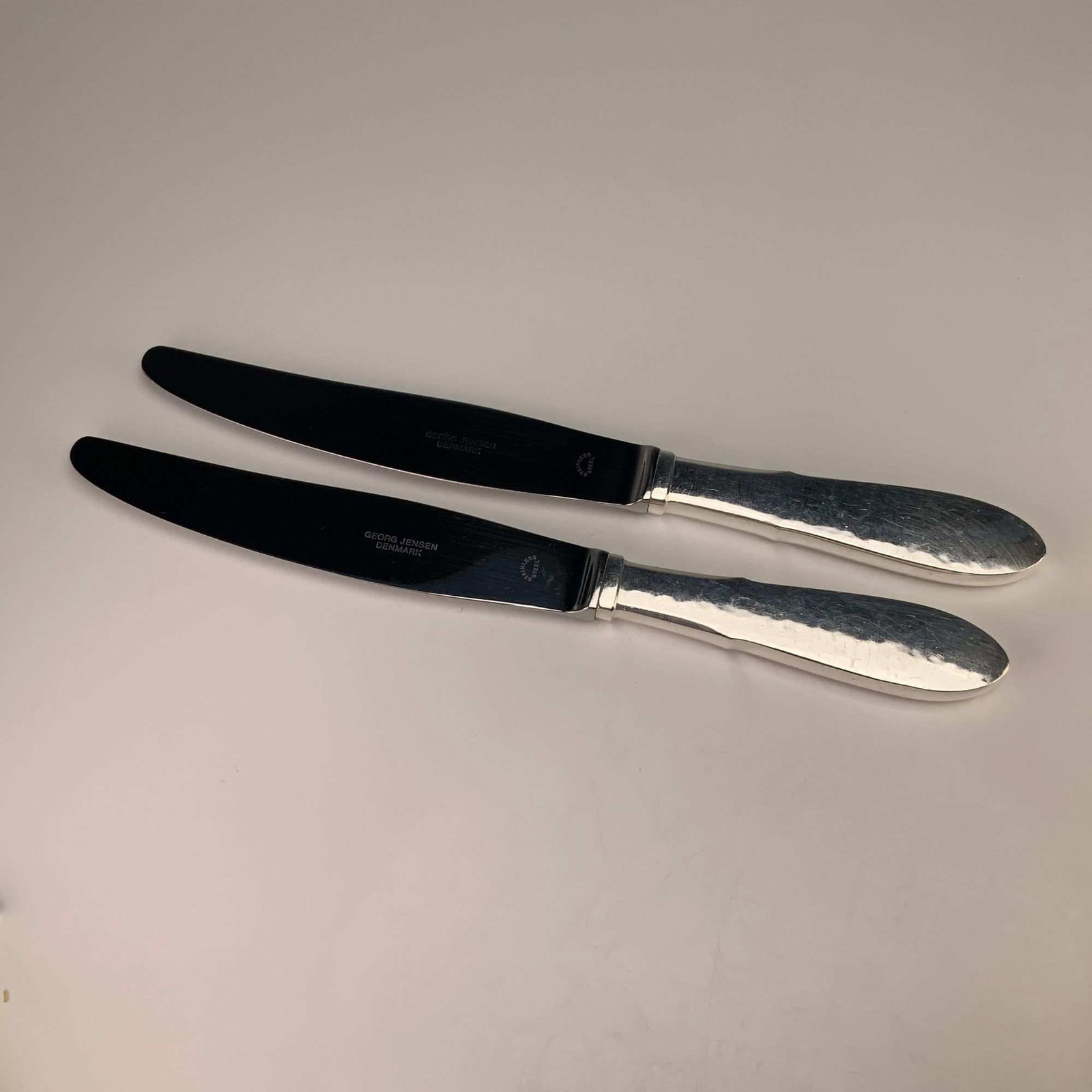 A Pair of Georg Jensen Denmark Mermaid Pattern EPNS Knives: This pair of knives is produced by Georg Jensen of Denmark in the Mermaid pattern. The pieces feature handles made of electro-plated nickel silver (EPNS) with a hand-hammered finish and rounded,