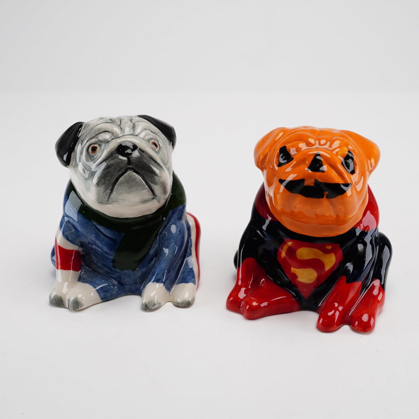 Lot of 2 Kevin Francis Face Pots Artist Edition Bulldogs, Pumpkin Superman and British Flag: This lot consists of a pair of two-piece glazed ceramic jars from the Kevin Francis Face Pots collection, designated as Artist Edition pieces. Each jar is modeled as a bulldog in a distinctive