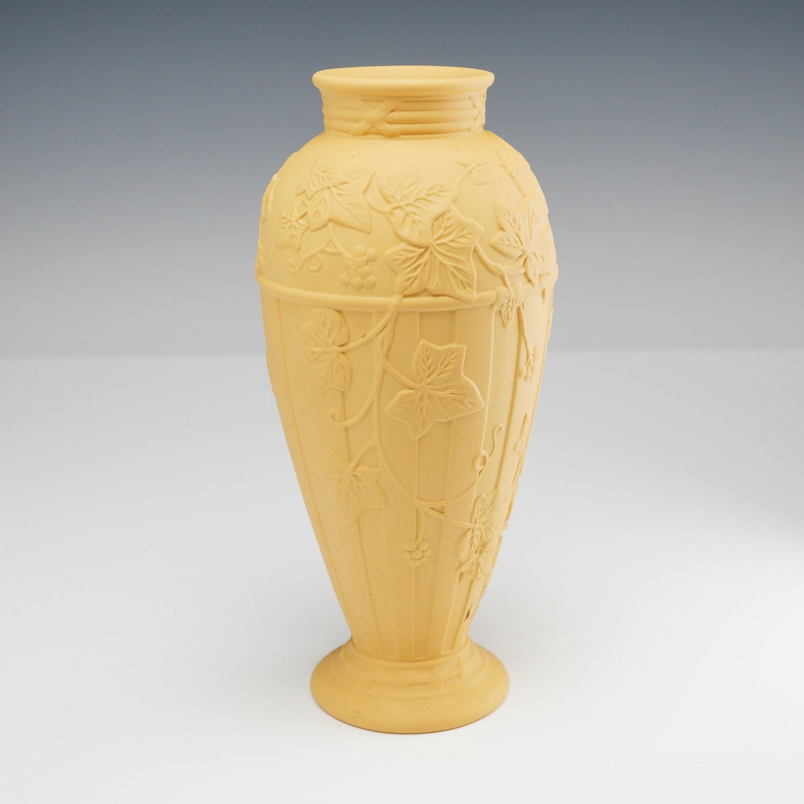 Wedgwood Yellow Jasperware Vase: This Wedgwood yellow jasperware vase is decorated in the Doric Ivy pattern. The vessel features a matte, unglazed finish in a Primrose yellow colorway. It is designed with a tapered ovoid body that