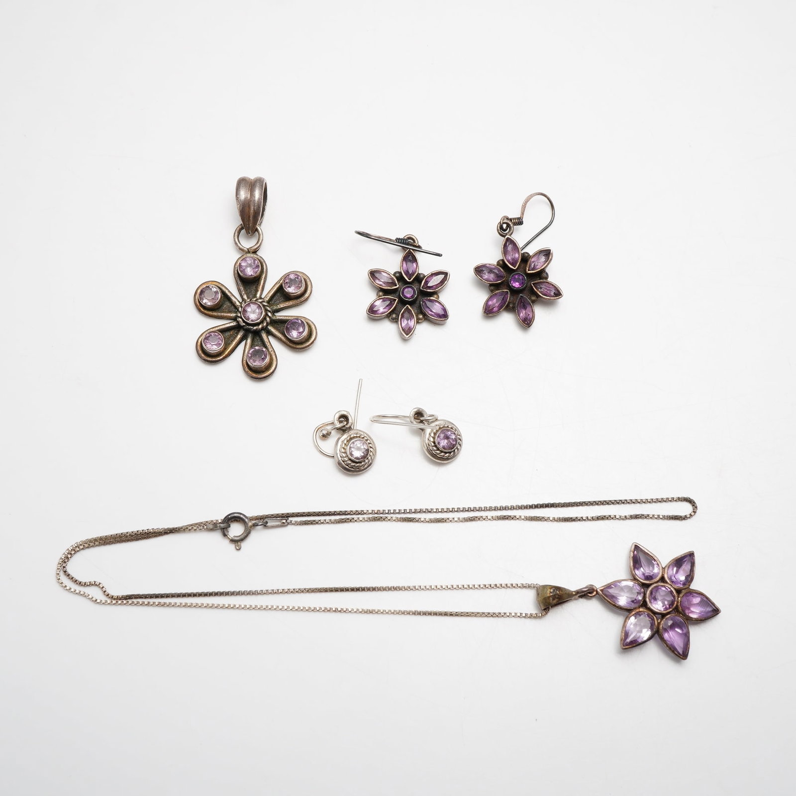 6pc Sterling Silver and Amethyst Jewelry Including Earrings, Pendant and Necklace: A 6pc sterling silver and amethyst gemstone jewelry collection featuring several floral-inspired designs. The group includes a large seven-petal openwork pendant set with a central round faceted ameth