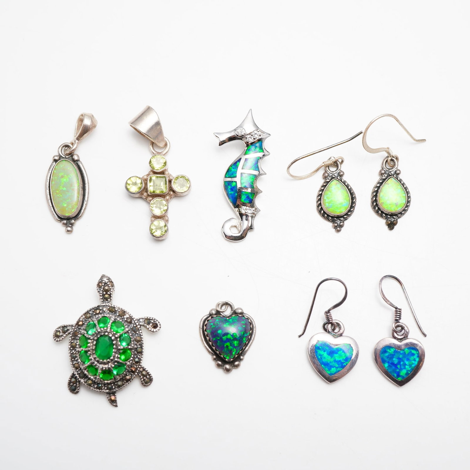 9pc Sterling Silver Gemstones Jewelry: 2 Pair of Earrings and 4 Pendants: This lot features a 9pc collection of sterling silver gemstones jewelry, including 2 pair of earrings and 4 pendants. The assortment focuses on designs incorporating simulated opal and faceted green g