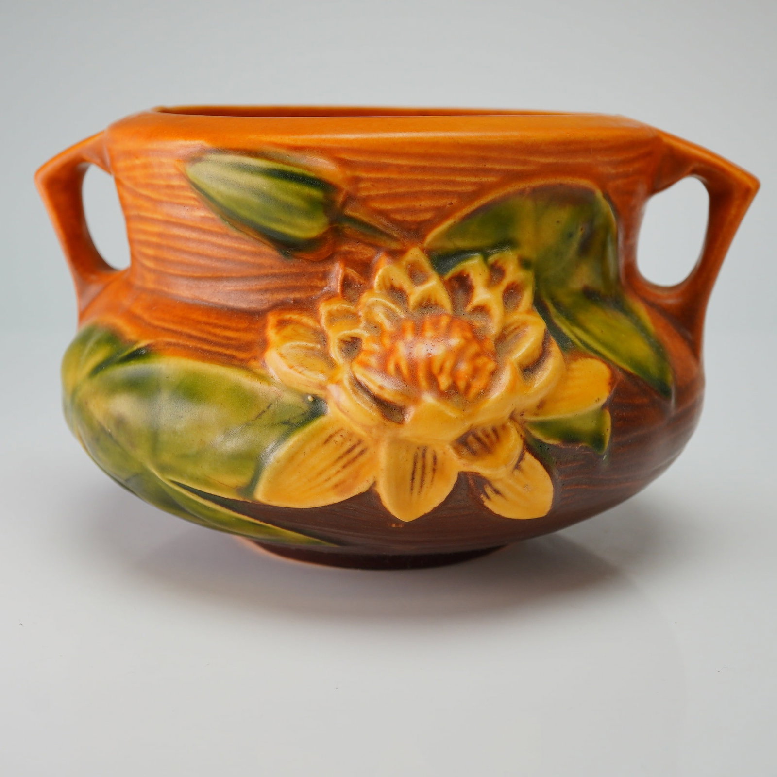 Roseville Pottery Brown Jardiniere, Water Lily: A Roseville art pottery ceramic jardiniere from the Water Lily pattern, introduced circa 1943. The vessel features a textured matte glaze with a high-relief embossed decoration of a yellow water lily 