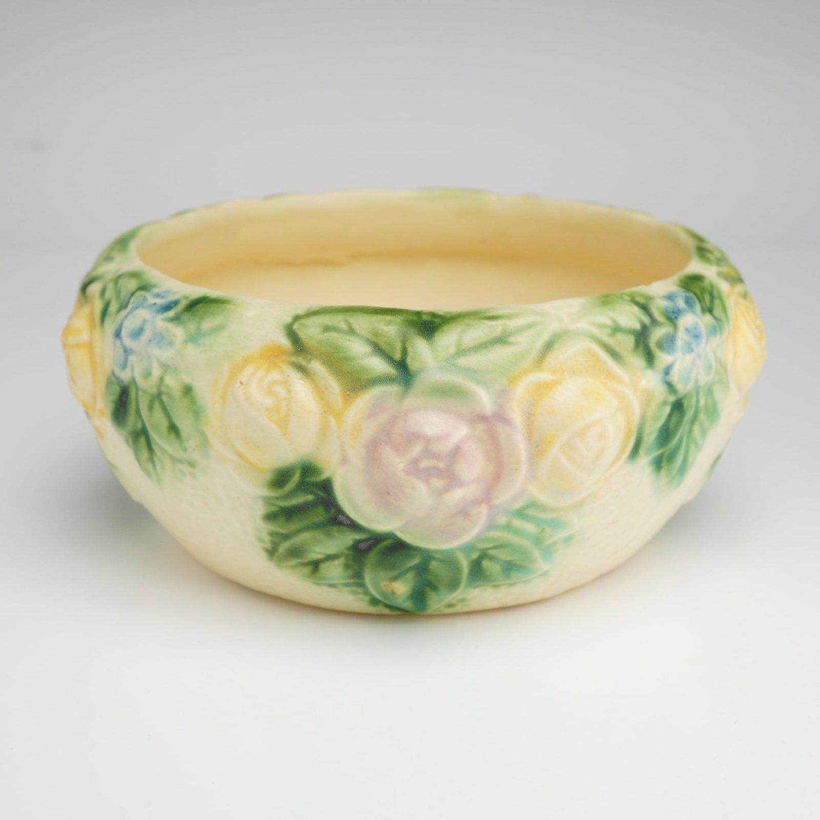 Roseville Pottery Creamware Floral Bowl, Rozanne 1917: This shallow, rounded bowl belongs to the Rozane line, specifically the Ivory floral variant introduced around 1917. The cream-colored earthenware body features a high-relief molded design of roses in