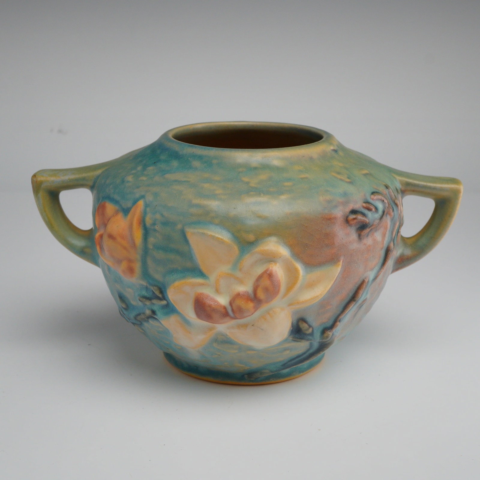 Roseville Pottery Two Handled Rose Bowl, Magnolia: This piece is from the Magnolia line, which was first introduced in 1943. The vessel features a squat, globular form, commonly identified as a rose bowl, flanked by two integral angular handles. The e