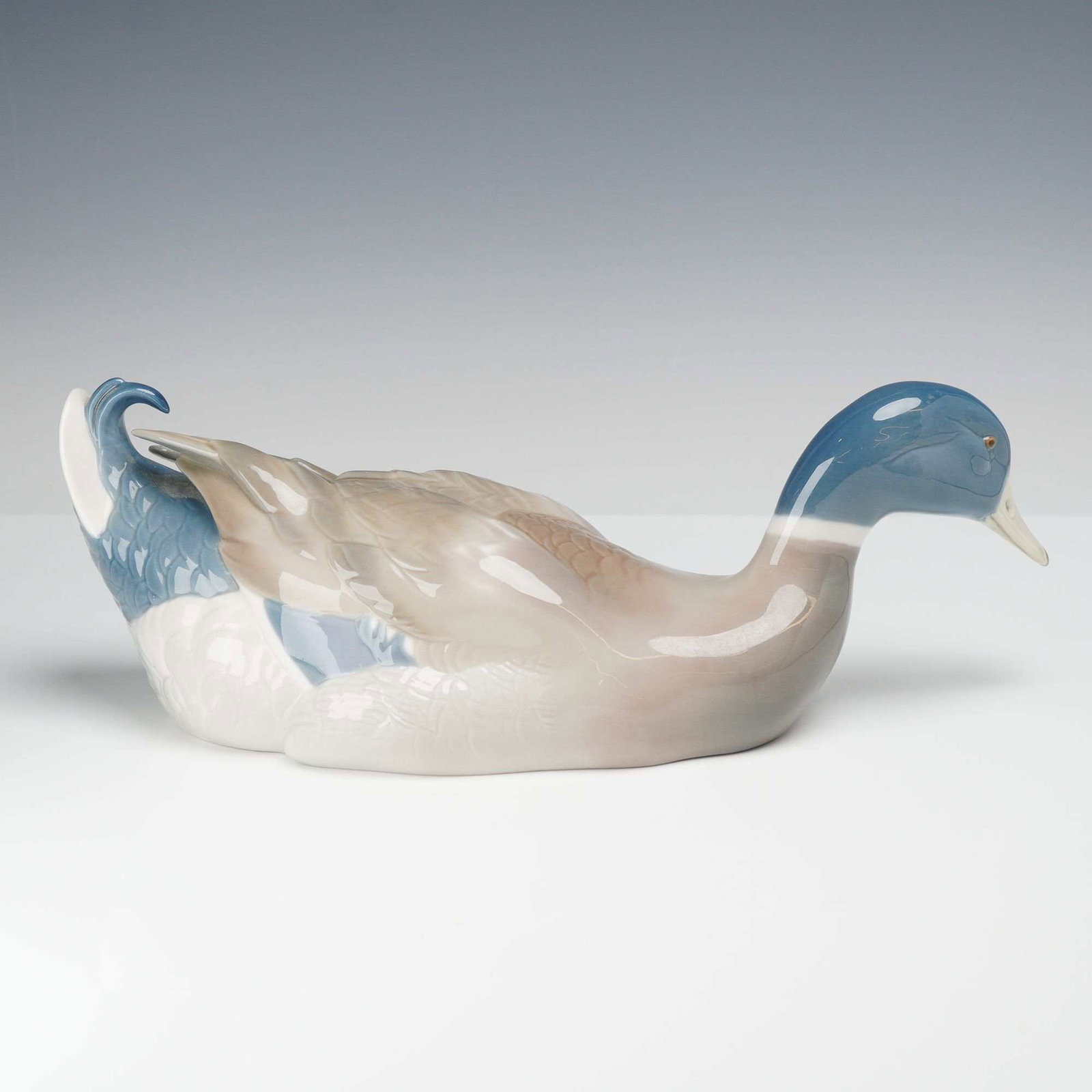 Lladro Porcelain Figurine, Mallard Duck 01005288: This Lladro porcelain figurine depicts a mallard duck (01005288) in a resting pose. The piece is crafted from glazed porcelain with a high-gloss finish. The decoration features a color palette charact