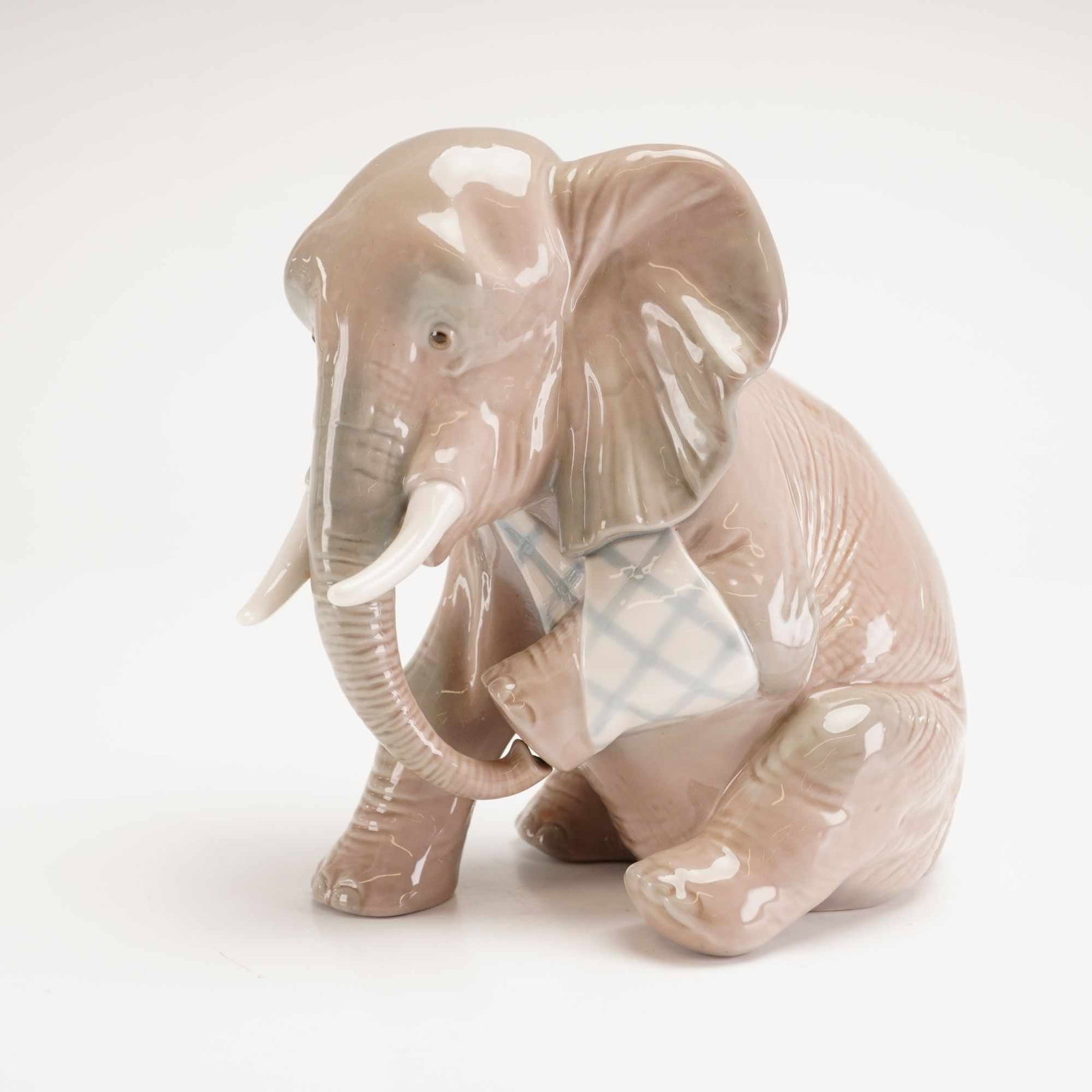 Lladro Porcelain Painful Elephant Figurine Number 5020: A Lladro porcelain figurine titled Painful Elephant, model number 5020. The figurine features a seated baby elephant finished in a high-gloss gray-tan glaze with white tusks. It is accented with a lig