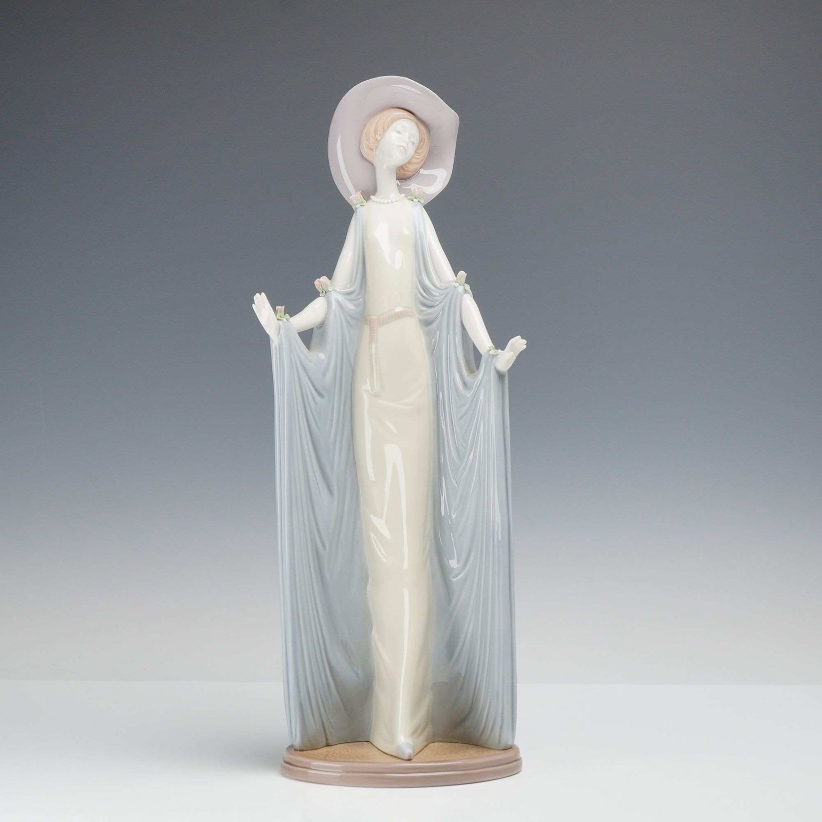 Lladro Porcelain Figurine, Afternoon Tea Number 01001428: A polychrome glazed porcelain figurine by Lladro titled Afternoon Tea, model number 01001428. The sculpture depicts an elegant, elongated female figure in a pale cream floor-length gown with a draped,