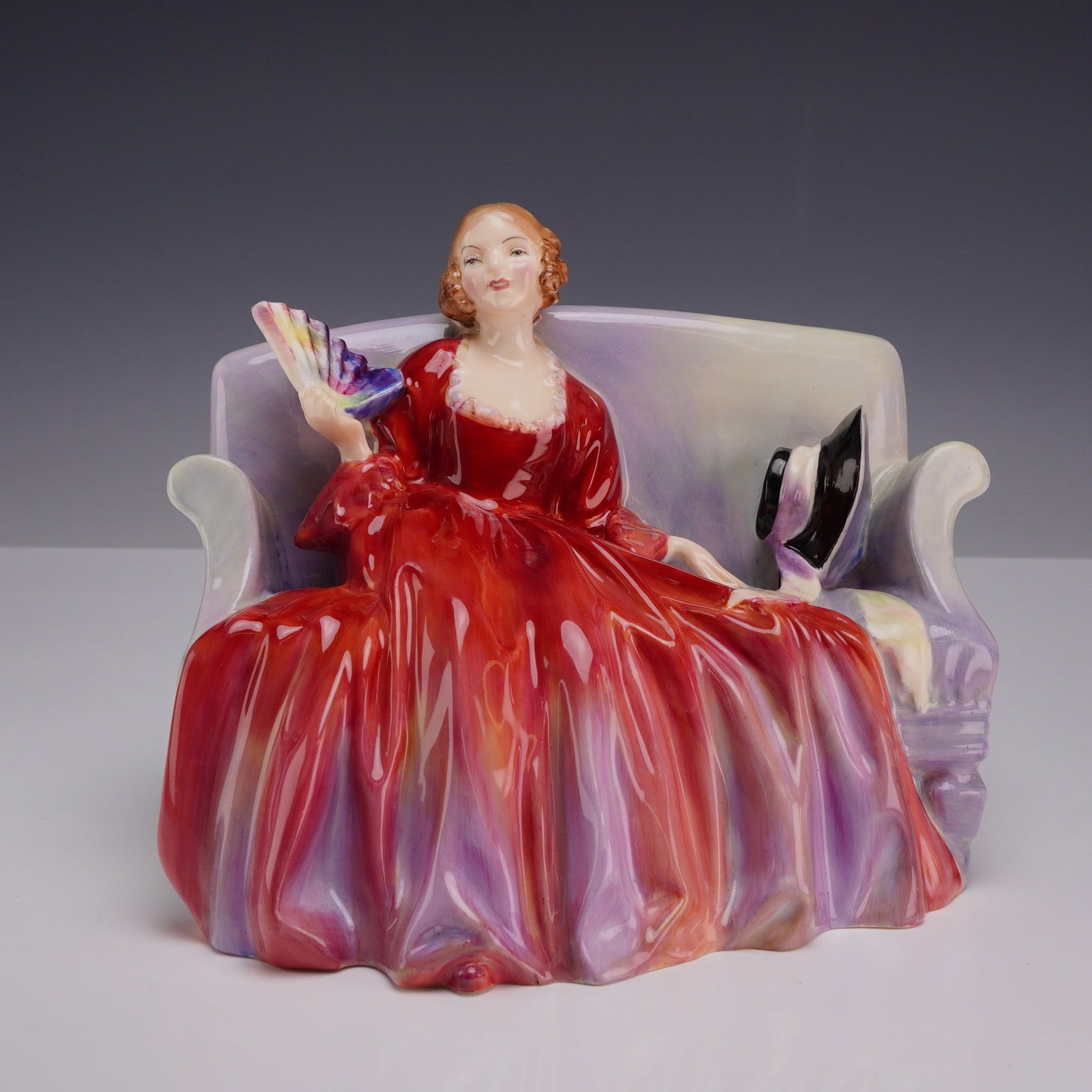 Royal Doulton Figurine, Sweet & Twenty HN 1298: A Royal Doulton glazed bone china figurine titled Sweet & Twenty, model number HN 1298. The figurine depicts a young woman seated on a high-backed settee wearing a voluminous red dress with iridescent