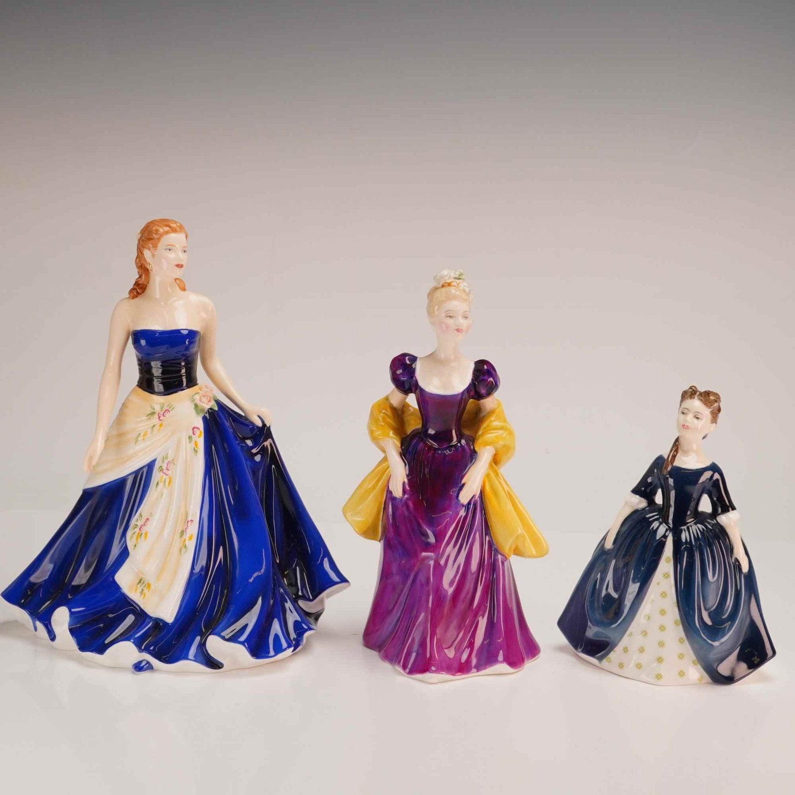 Three Royal Doulton Bone China Figurines Olivia HN5114, Loretta HN2337 and Debbie HN2385: This lot features three glazed bone china figurines from Royal Doulton, including models from the Pretty Ladies and classic collections. The first figurine is Olivia, HN 5114, the Figure of the Year 2