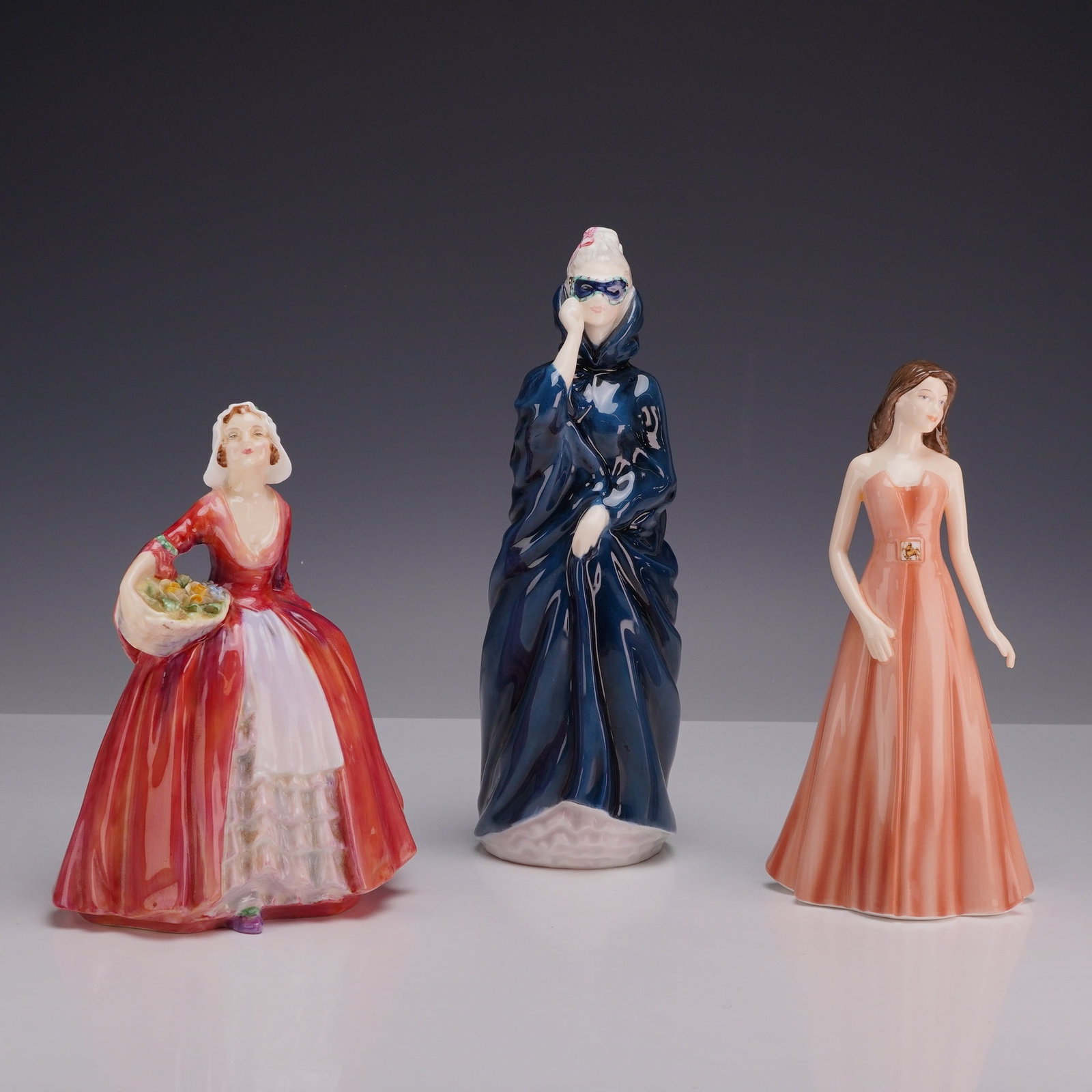 3pc Royal Doulton Bone China Figurines, Janet, Masque, and Sagittarius: This collection consists of three Royal Doulton glazed bone china figurines. Janet HN 1537 depicts a woman dressed in a red gown with a white apron and cap, holding a basket of flowers. Masque HN 2554