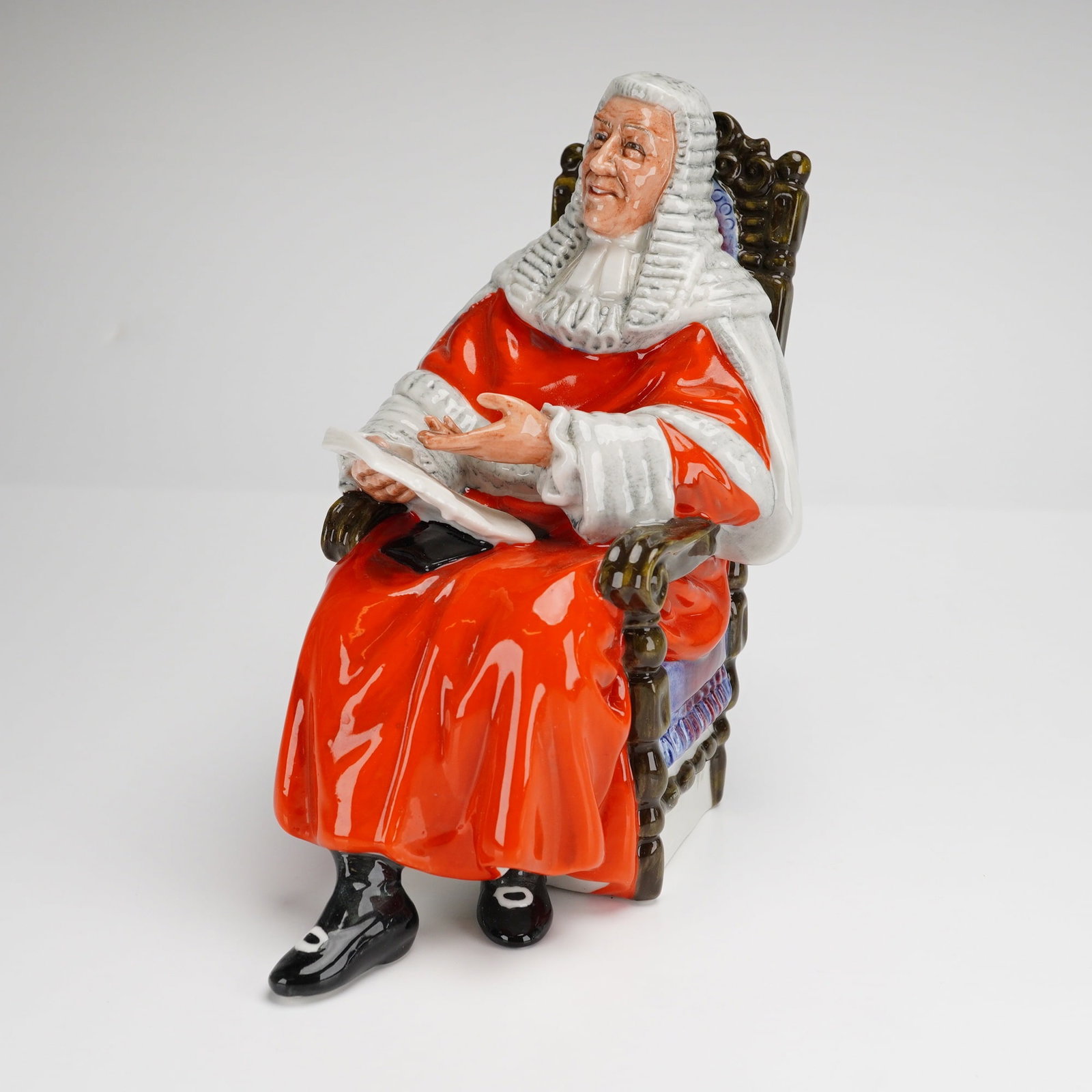 Royal Doulton Figurine The Judge HN2443: A Royal Doulton porcelain figurine titled The Judge HN2443. This glazed porcelain piece depicts a seated male figure in traditional judicial attire, featuring a long tiered white wig and a white jabot
