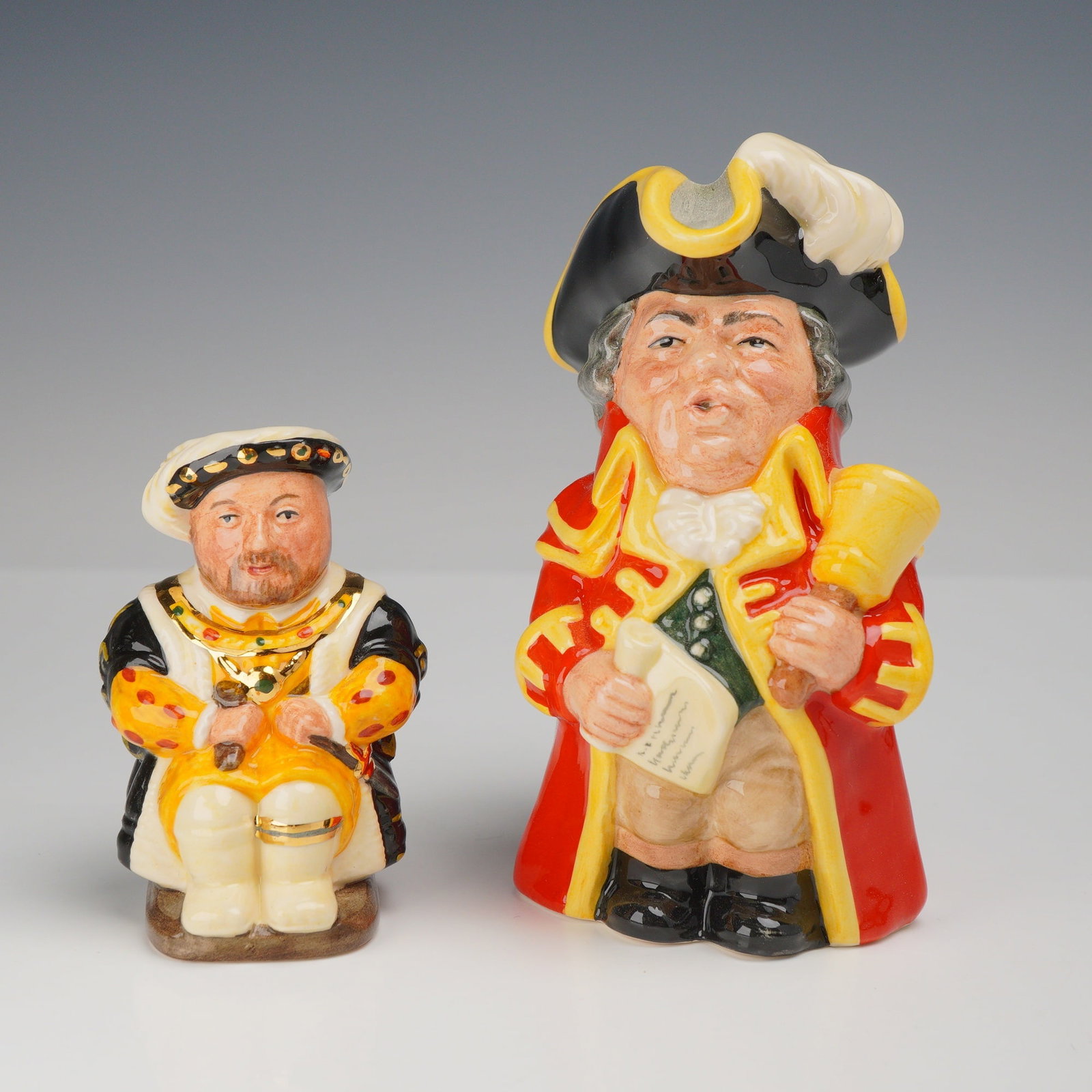 2pc Royal Doulton Limited Edition Character Toby Jugs Town Crier D6920 and King Henry VIII D7047: This lot features two limited edition character jugs produced by Royal Doulton. Both pieces are crafted from glazed ceramic with hand-painted polychrome details and gilded accents. The first jug depic