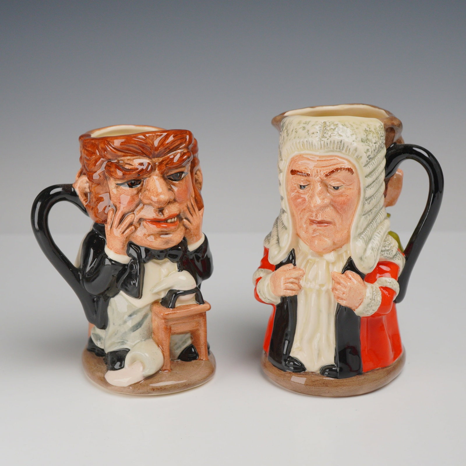 2pc Royal Doulton Two-Sided Character Jugs, Dr. Jekyll and Mr. Hyde D7024 and The Judge and Thief: This lot consists of a pair of hand-painted glazed ceramic two-sided character jugs produced by Royal Doulton, both designed by Stanley James Taylor. Each jug features two distinct characterizations o