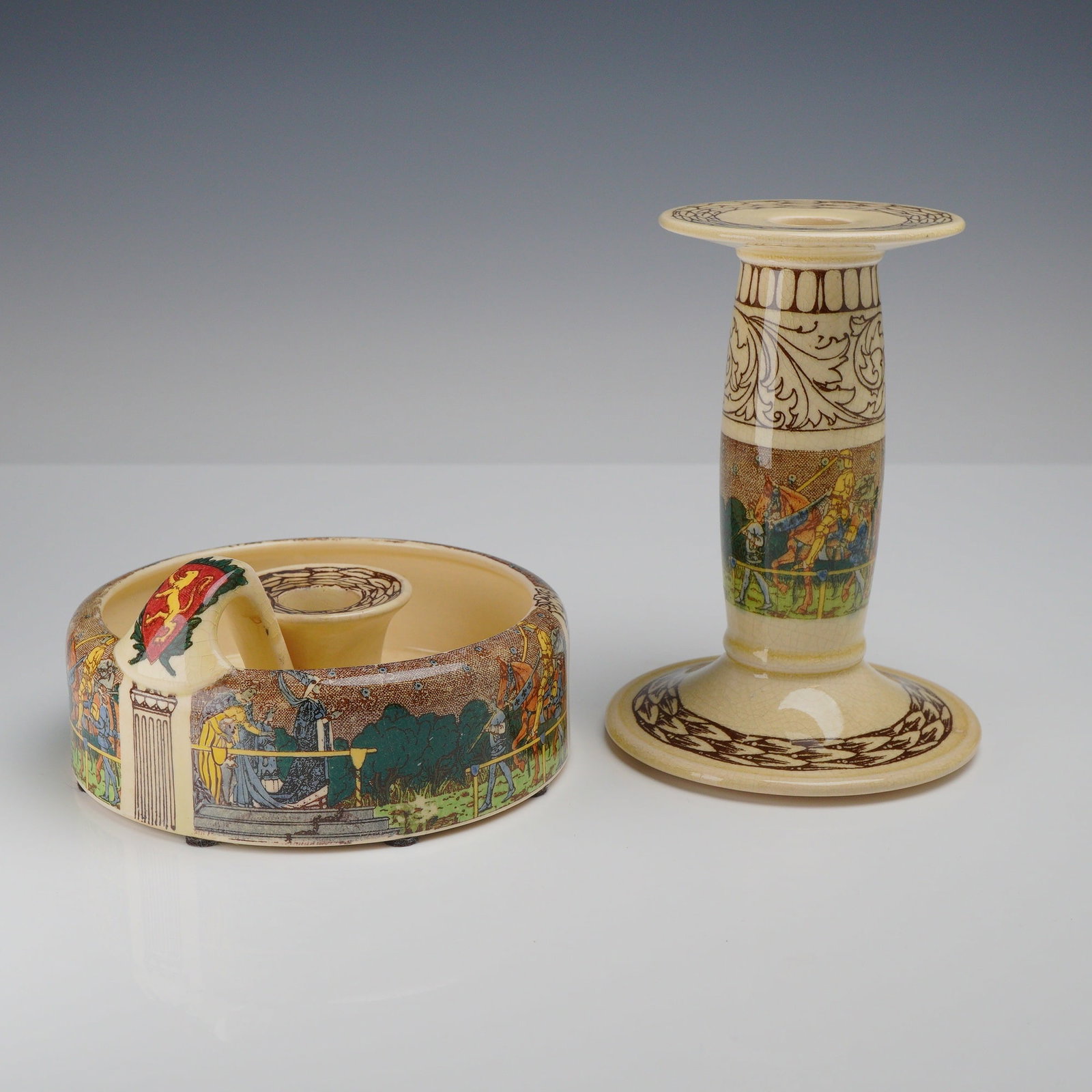 2pc Royal Doulton King Arthur's Knights Seriesware Candlesticks: This pair of Royal Doulton Seriesware ceramics in the "King Arthur's Knights" pattern (D2961) features medieval jousting scenes on glazed cream-colored earthenware. The set includes a tall column-form