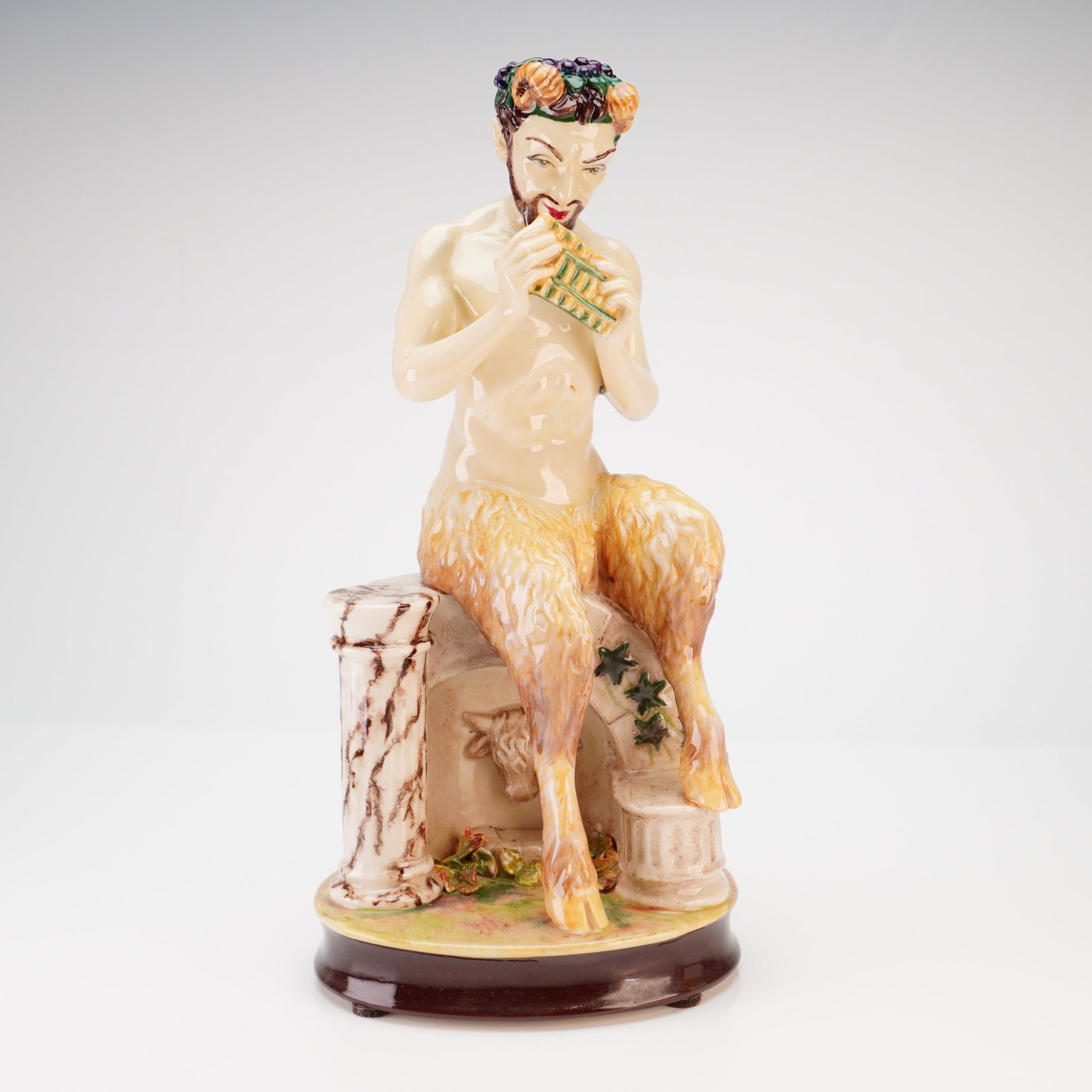 Kevin Francis Ceramics Limited Edition Pan Figurine by Andy Moss: A glazed polychrome ceramic figurine in the Art Deco style depicting Pan, the Greek god of the wild. The figure is shown seated upon a classical architectural ruin featuring a column and a relief of a