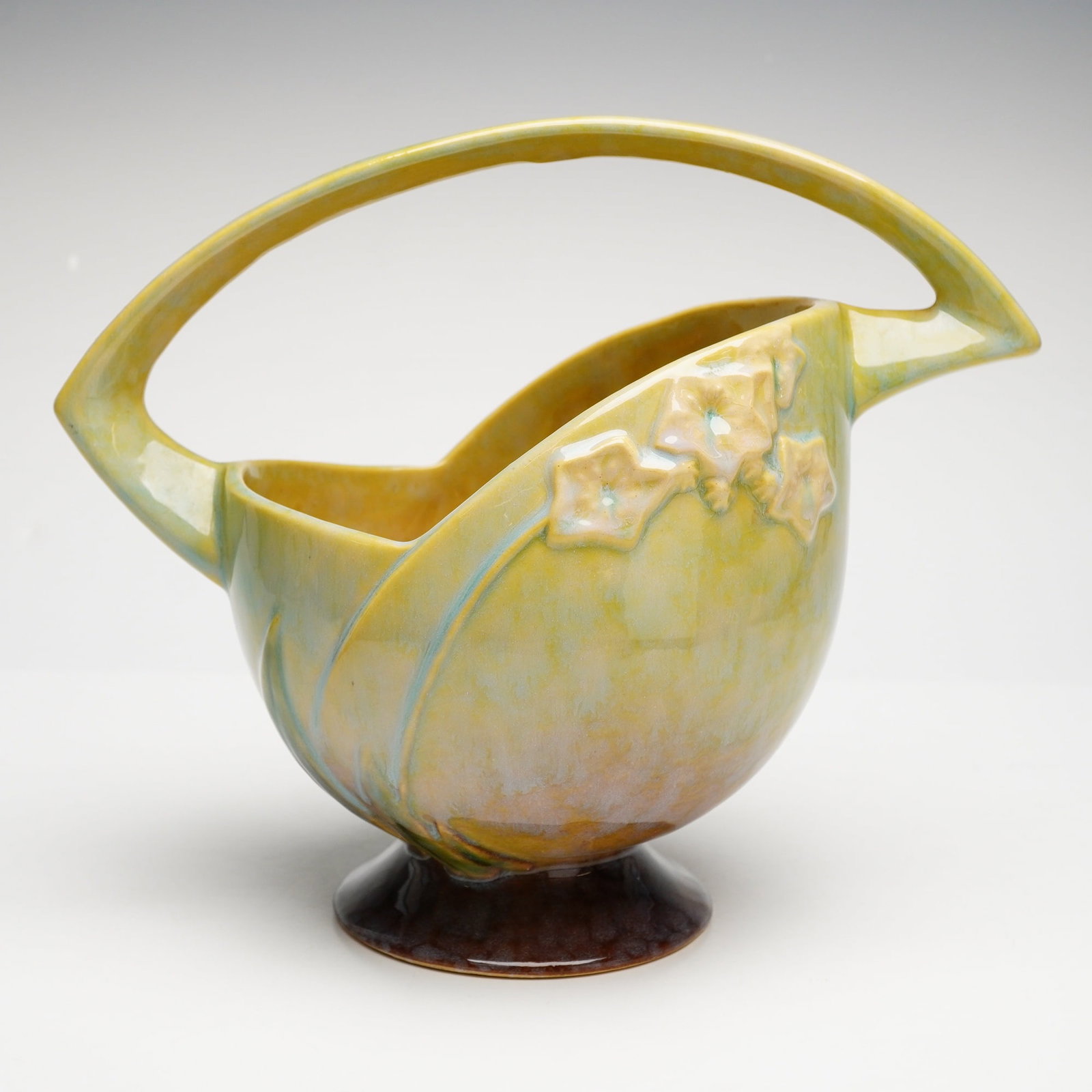 Roseville Pottery Floral Basket, Wincraft Chartreuse: This piece belongs to the Wincraft line, introduced in 1948, which updated traditional floral motifs with sleek, modern silhouettes. The vessel features a globular body with a distinctive asymmetrical