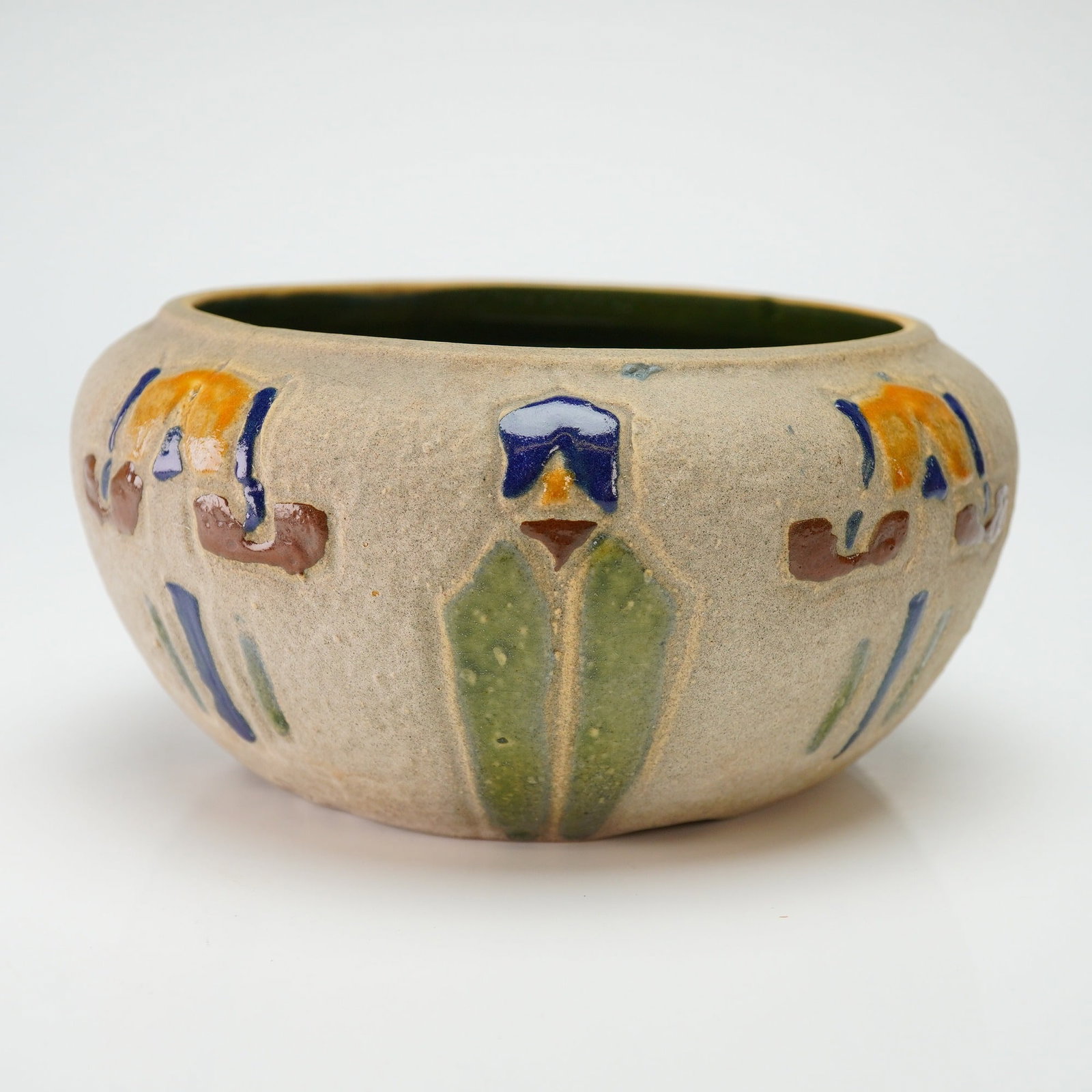 Roseville Pottery Bowl, Mostique: The Mostique pattern, introduced circa 1916. The vessel features a squat, rounded form with a textured, matte-beige exterior glaze. The exterior is decorated with raised, tube-lined stylized floral mo