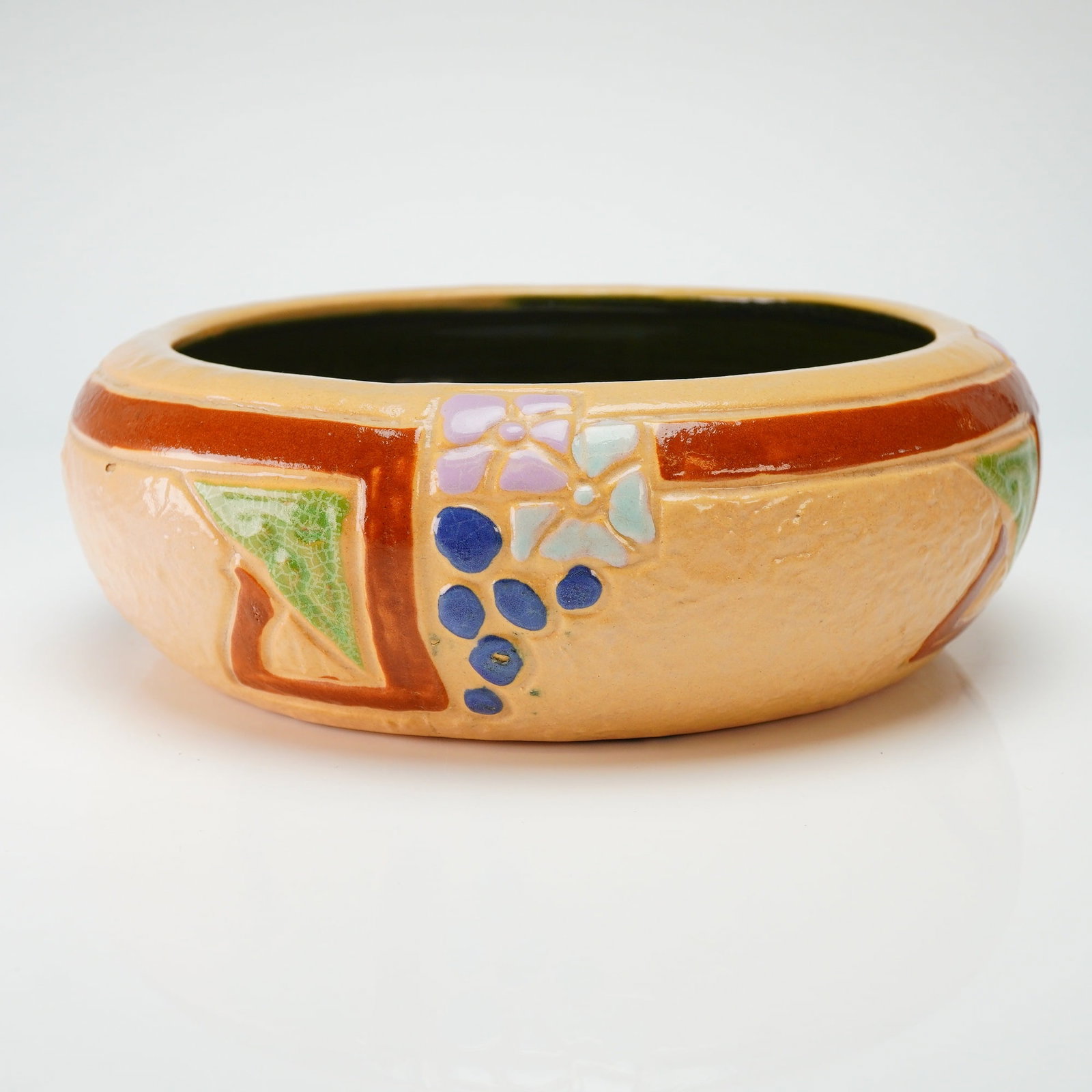 Roseville Tan Pottery Bowl, Mostique: Mostique pottery bowl featuring a textured tan exterior ground. The vessel is decorated with hand-painted stylized floral motifs including pink and light blue flowers alongside clusters of blue berrie