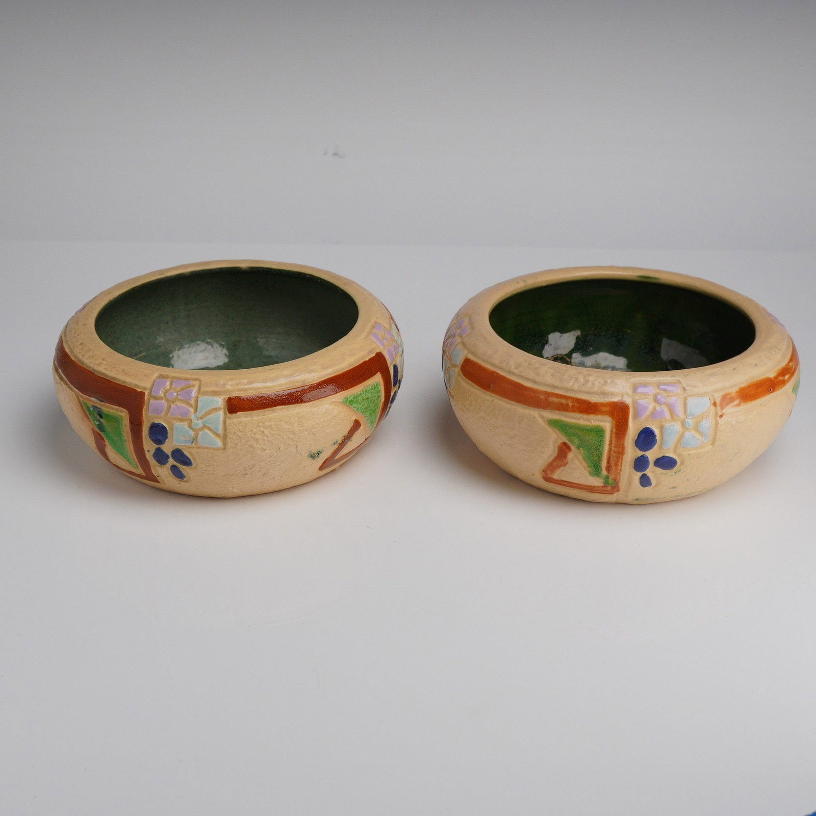 Pair of Roseville Tan Art Pottery Bowls, Mostique: The Mostique pattern was introduced in circa 1915. These circular ceramic vessels feature a textured, matte tan exterior decorated with hand-painted geometric and floral motifs in shades of orange, gr