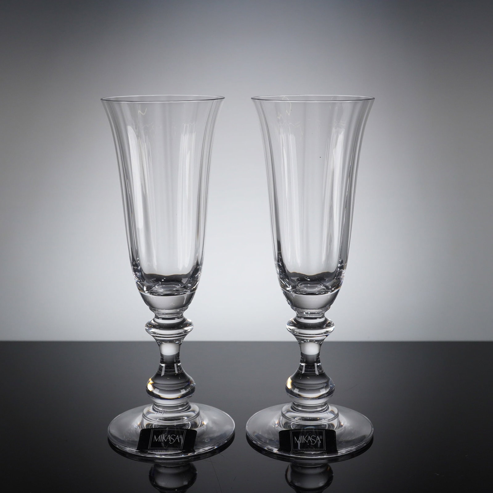 2pc Mikasa French Countryside Champagne Flutes: A pair of champagne flutes manufactured by Mikasa in the "French Countryside" pattern. The glasses are crafted from clear crystal and feature a tall, slender bowl with subtle vertical faceting around 
