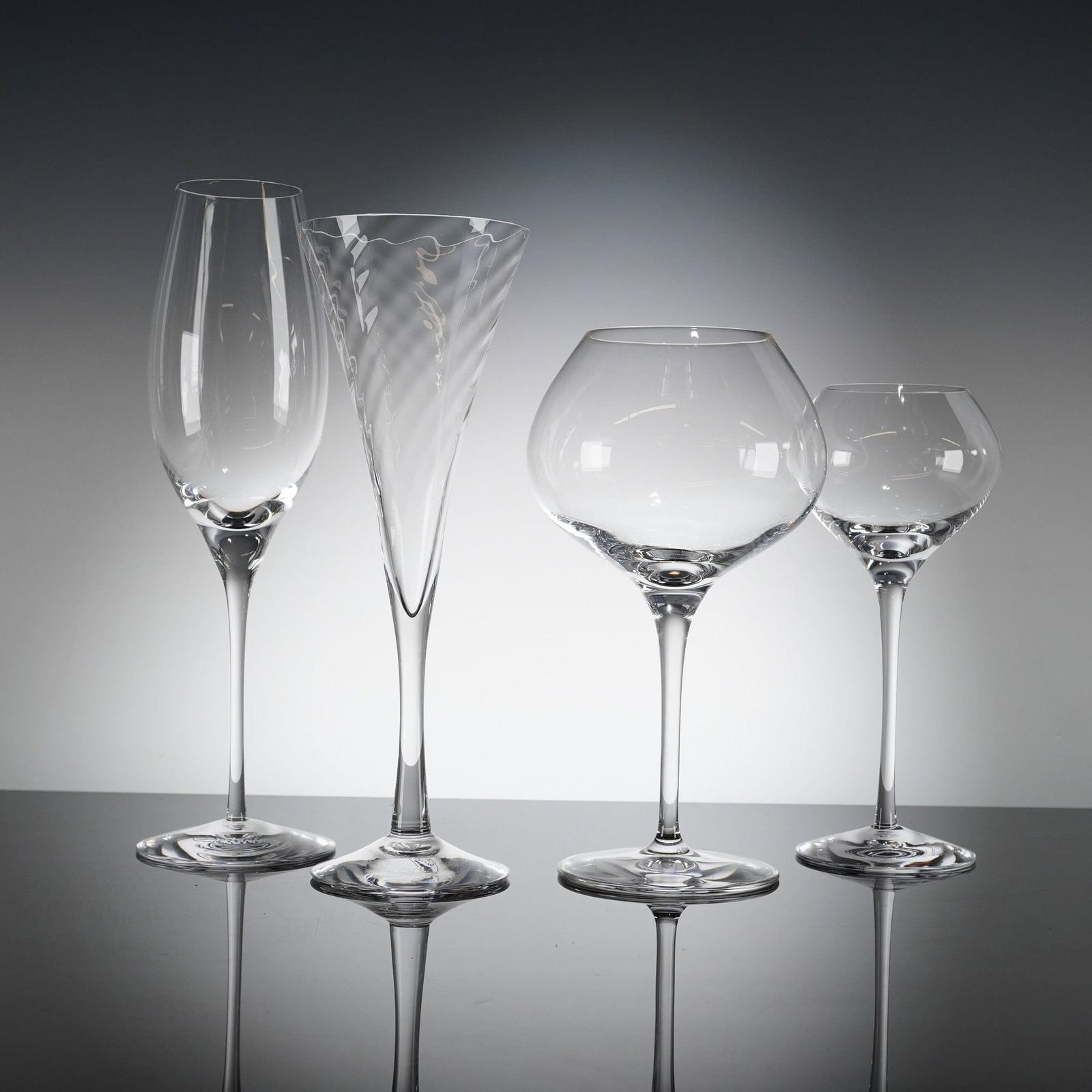 A Collection of 4 Orrefors Sweden Crystal Stemware Glasses: A collection of 4pc Orrefors Crystal glasses, featuring four distinct modern stemware styles. The collection includes one traditional champagne ?ute, one very tall V-shaped ?ute featuring prominent in