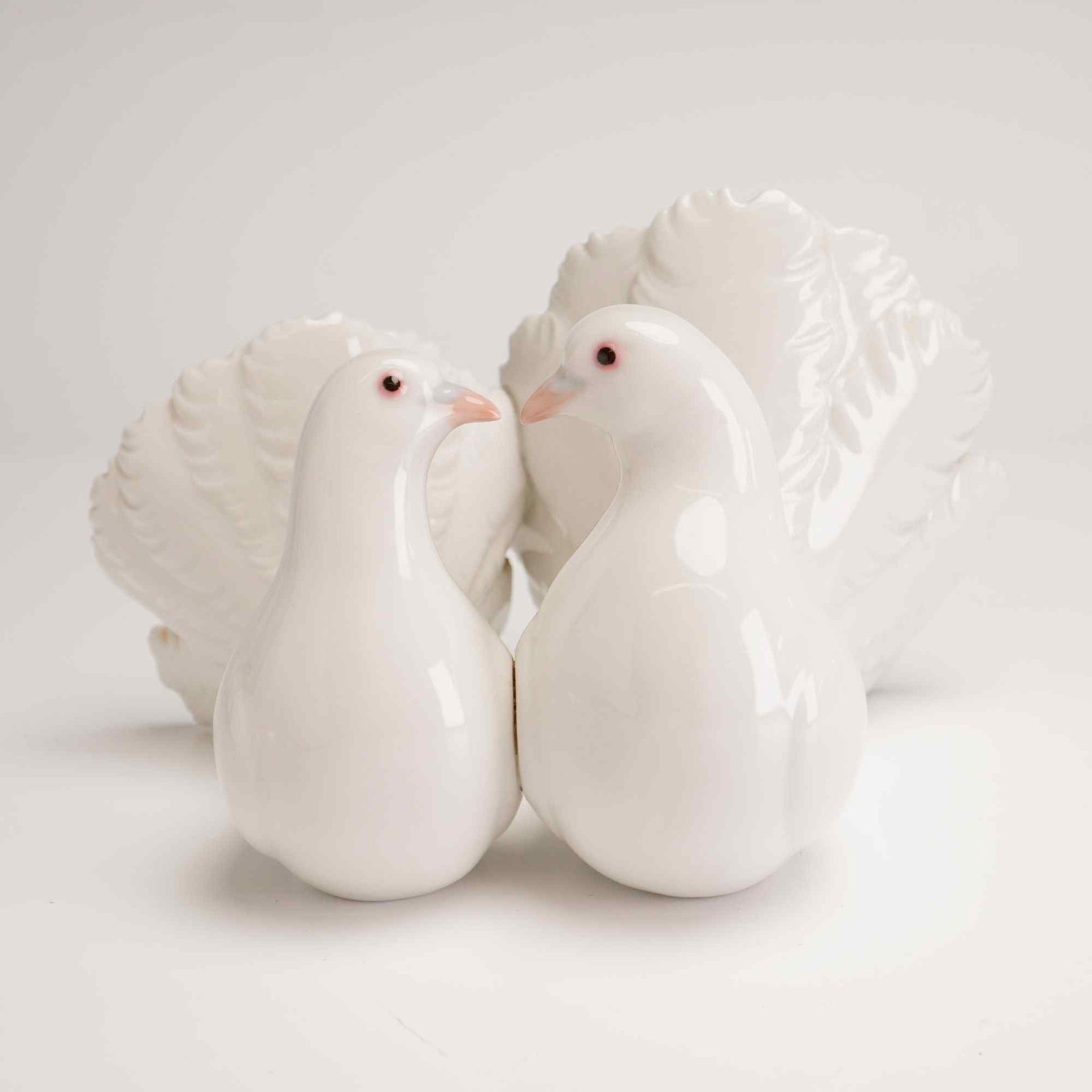 Lladro Glazed Porcelain Figurine Couple of Doves 01001169: The figurines are crafted in high-gloss white porcelain with prominent, fanned tails featuring molded, scalloped feather details. The birds are designed in a mirrored arrangement to face one another, 