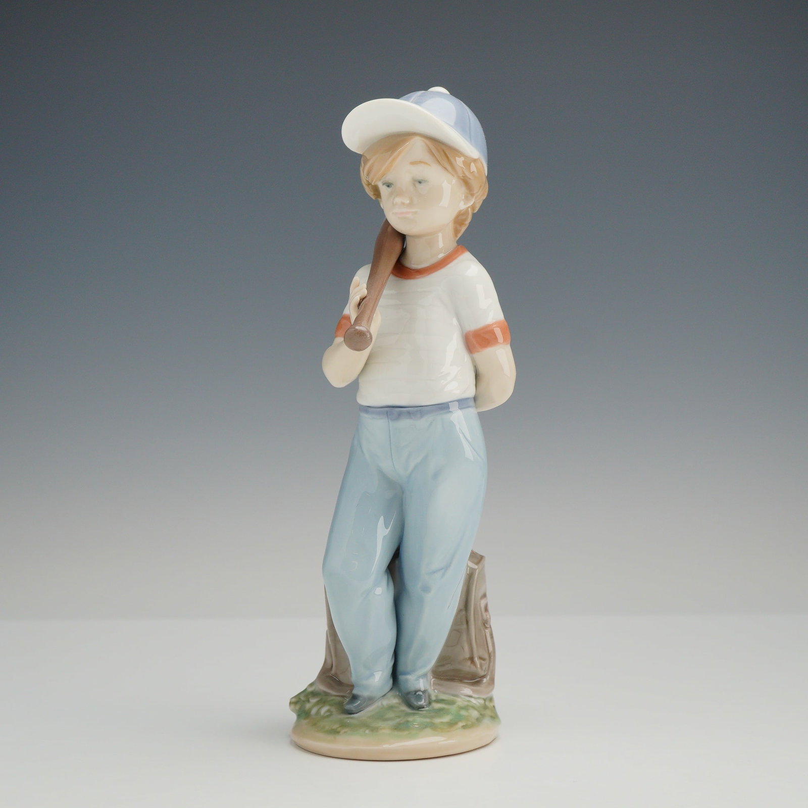 Lladro Glazed Porcelain Figurine, Can I Play ? 7610: This glazed porcelain figurine titled "Can I Play?" model number 7610, was designed by sculptor Antonio Ramos and issued for the Collectors Society in 1990. The figure captures a young boy in a baseba