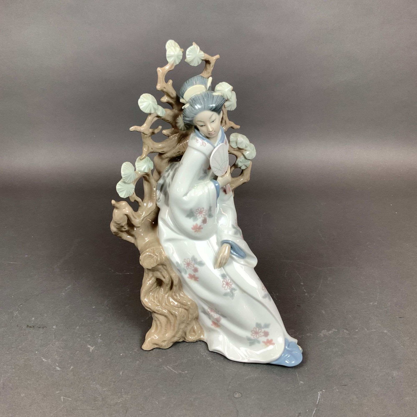 Lladro Glazed Porcelain Figurine, Japanese Girl with Fan 4807: A Lladro glazed porcelain figurine titled Japanese Girl with Fan, model number 4807. Designed by sculptor Vicente Mart?nez, this piece depicts a woman in a traditional kimono featuring a soft pastel f