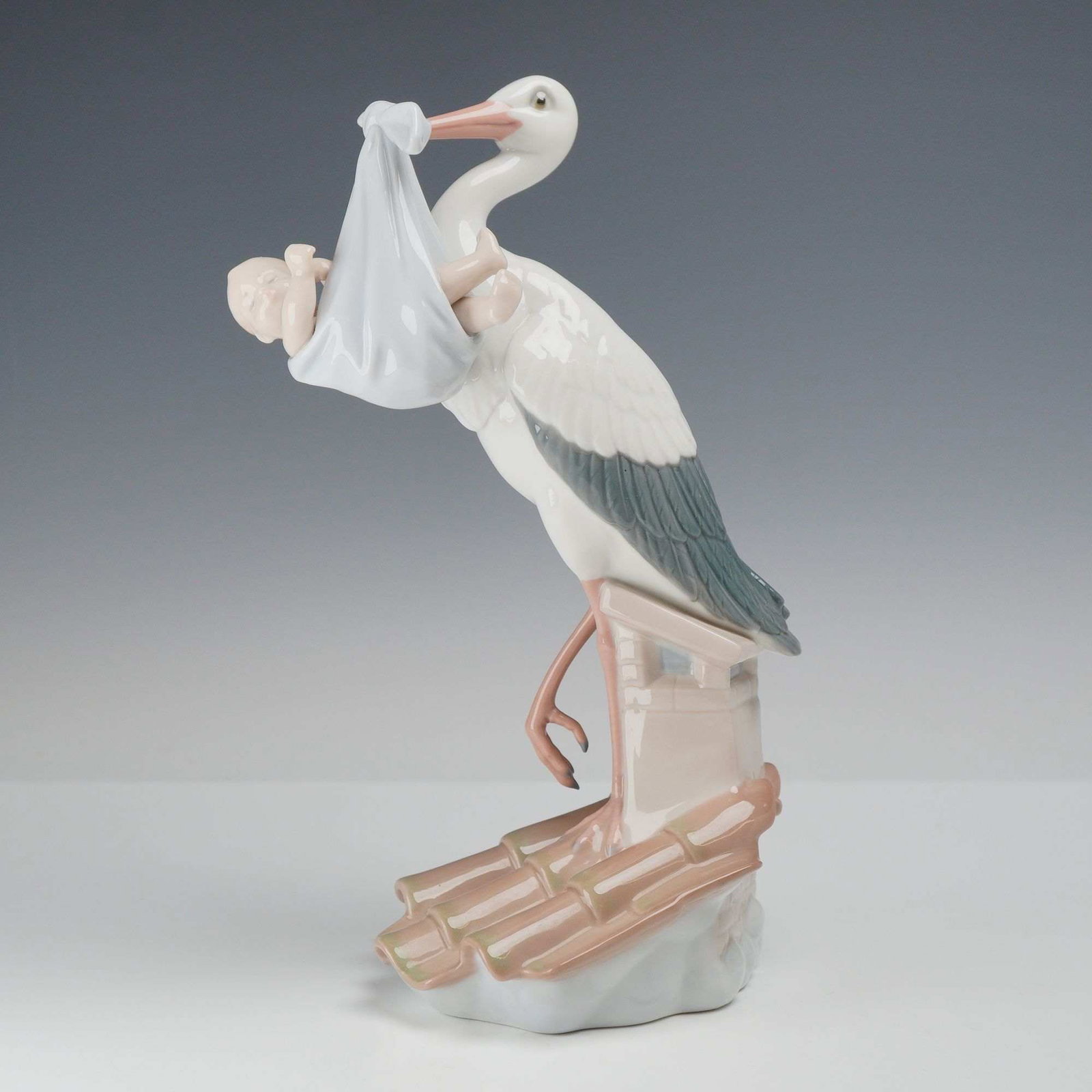 Lladro Porcelain Figurine, A Special Gift 01006228: This Lladro glazed porcelain figurine is titled Special Gift, also known by the model number 01006228. The piece depicts a white stork with gray-blue wing feathers perched upon a chimney on a terracot
