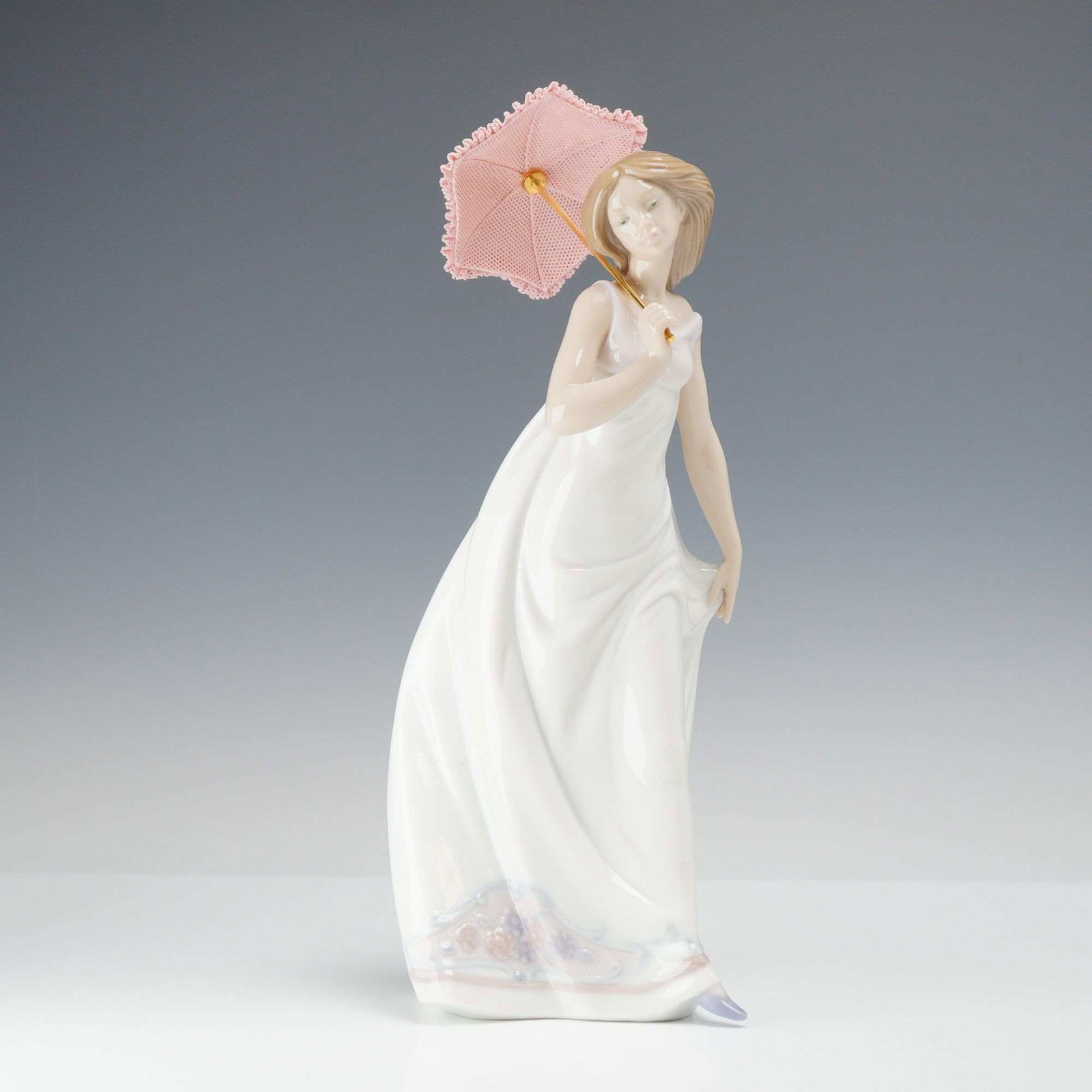 Lladro Porcelain Figurine, Afternoon Promenade 01007636: Lladro glazed porcelain figurine titled Afternoon Promenade, model number 01007636. The piece features a young woman in a sleeveless, floor-length white gown, holding a pink parasol over her right sho