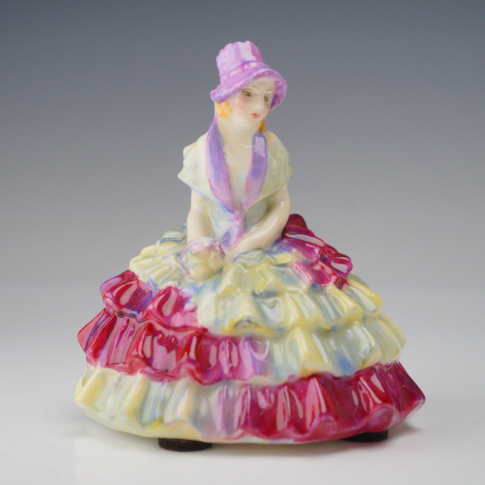 Royal Doulton Porcelain Miniature Figurine, Chloe M29: A miniature glazed porcelain figurine titled Chloe, model number M29, manufactured by Royal Doulton. The Art Deco style figure depicts a seated young woman wearing a wide-brimmed sun hat in shades of 