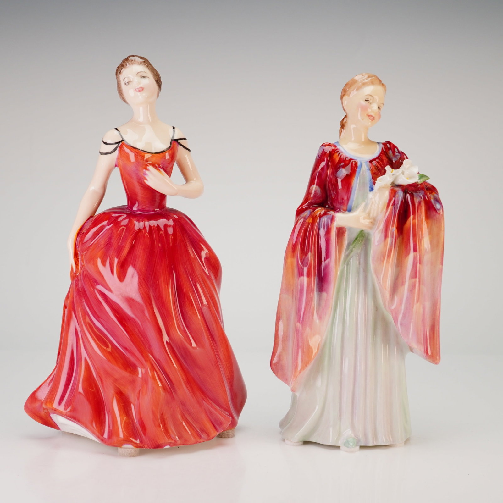 2pc Royal Doulton Bone China Figurines, Innocence HN 2842 and Olivia HN1995: This lot features two Royal Doulton glazed bone china figurines. The first figurine, titled Innocence (HN 2842), depicts a woman in a floor-length red gown with black shoulder straps and her hair styl