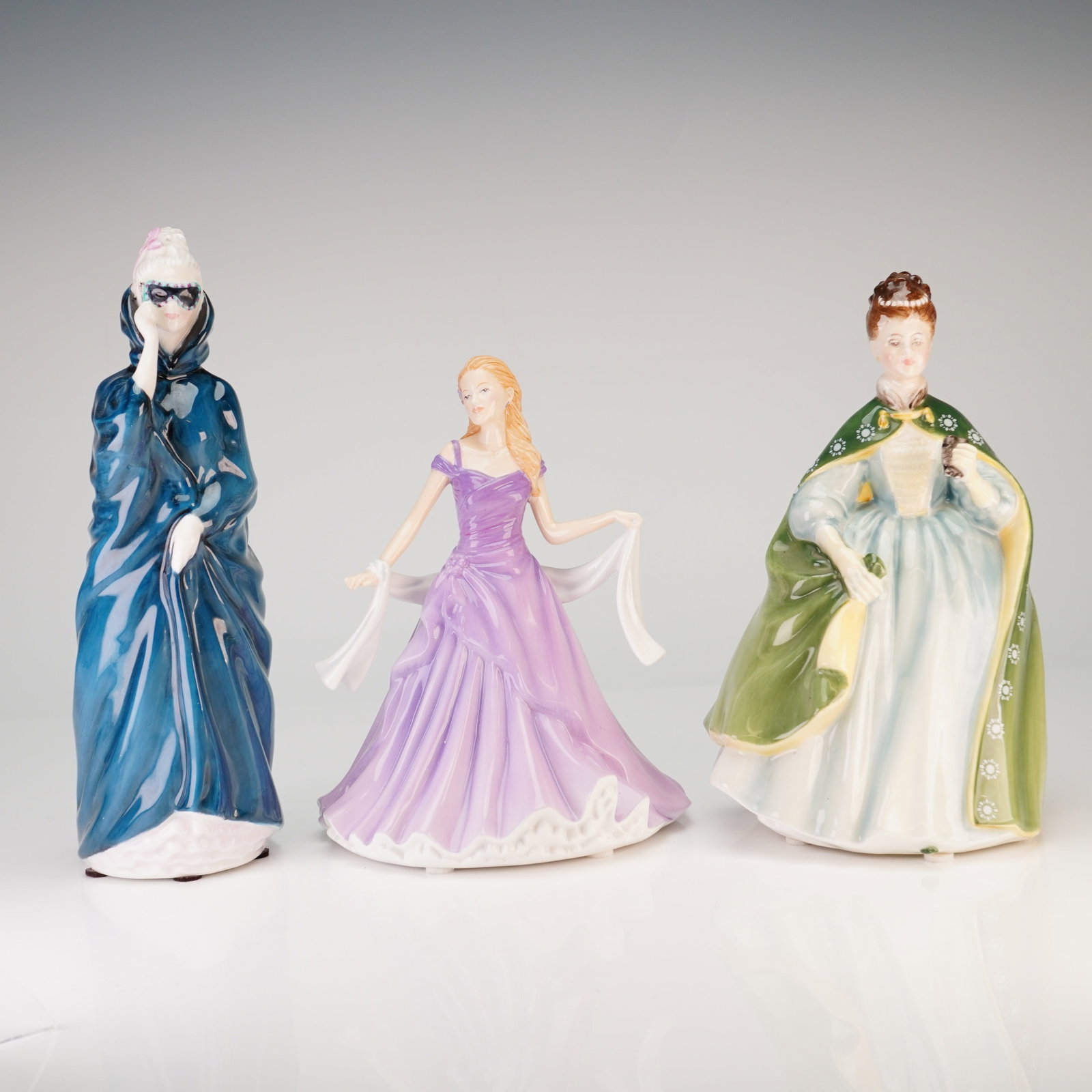 3pc Royal Doulton Bone China Figurines, Masque, Premiere and Amanda: This lot consists of three glazed bone china figurines produced by Royal Doulton. The collection features Masque, model HN 2554, depicting a woman in a dark blue hooded cloak wearing a black mask; Pre